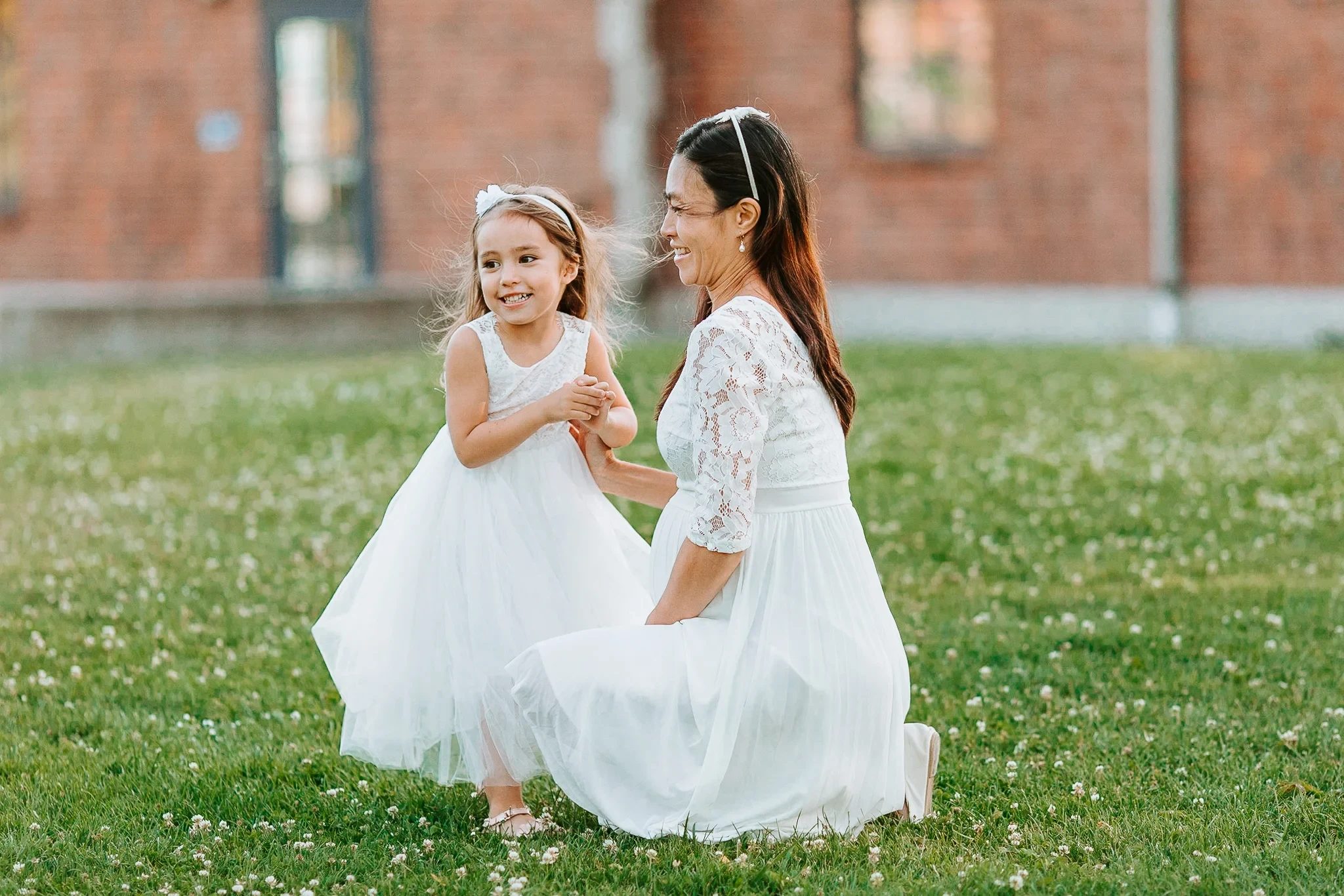 Woman and child in white dresses sit together on a green lawn