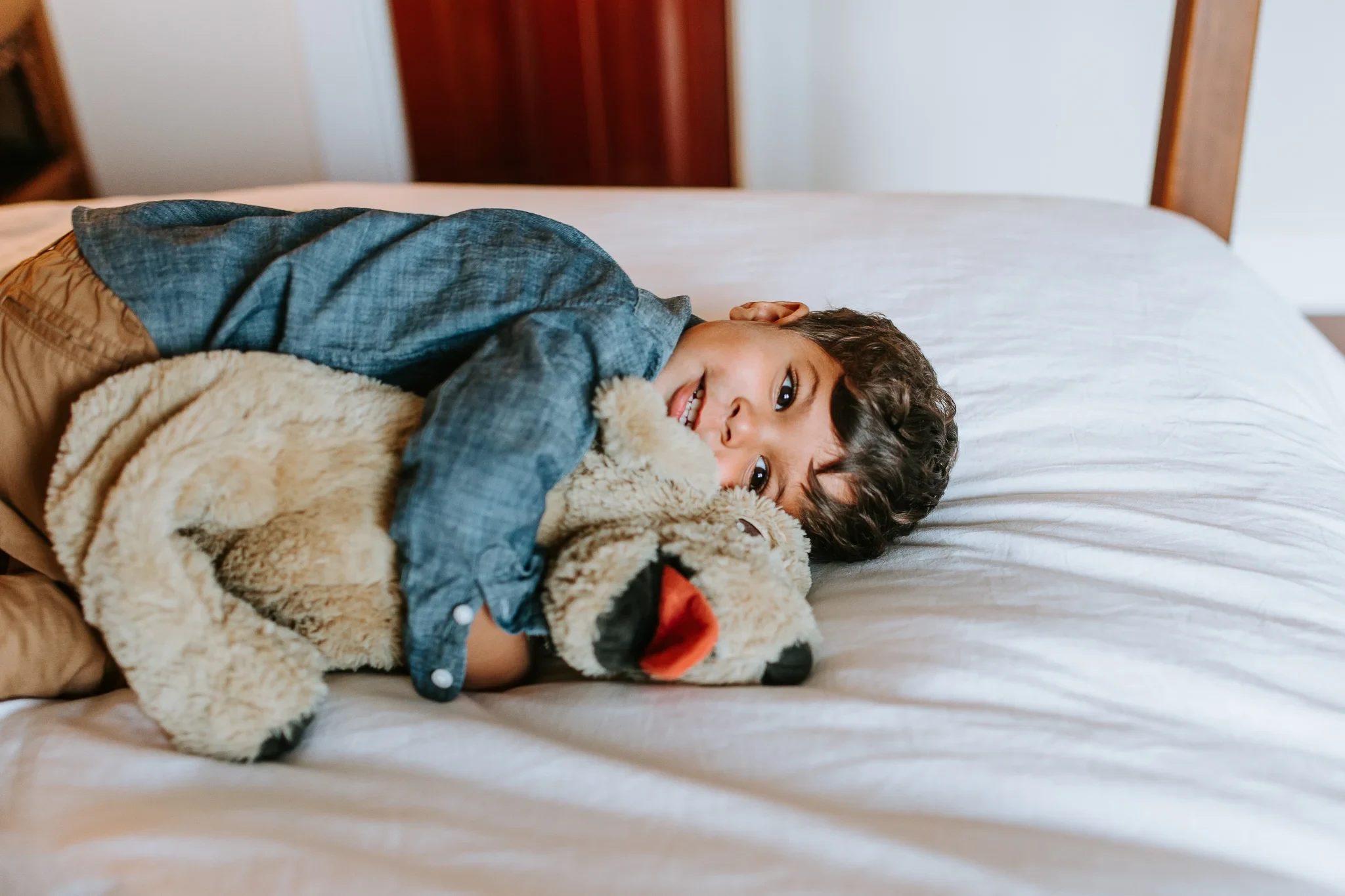 Child lies on a white bed beside a soft toy