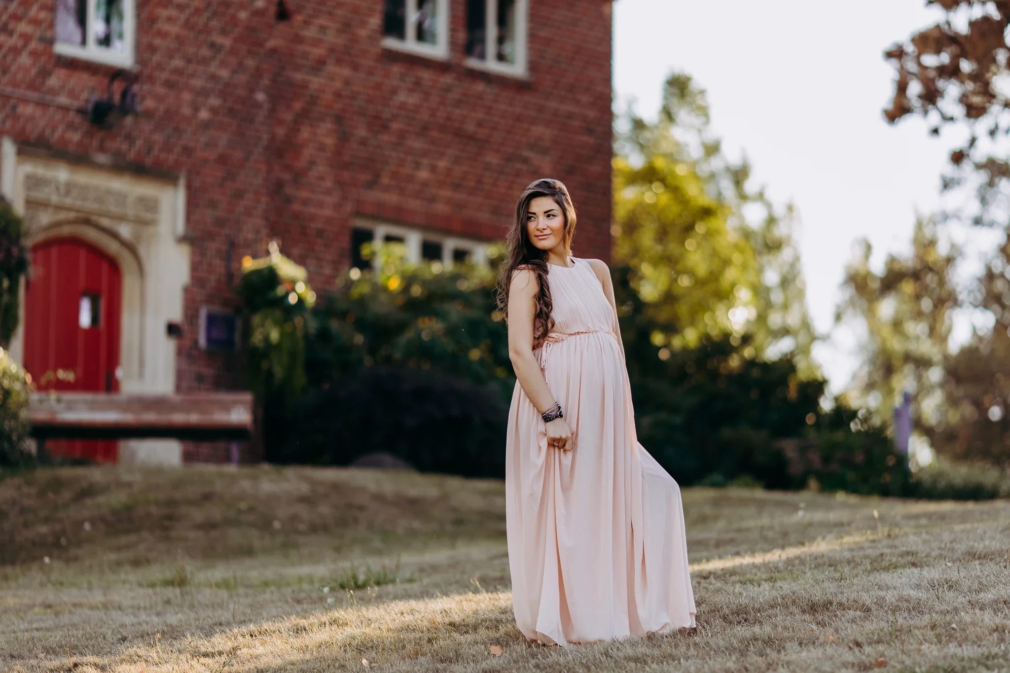Full-length portrait of a woman in a long pink dress beside a brick building