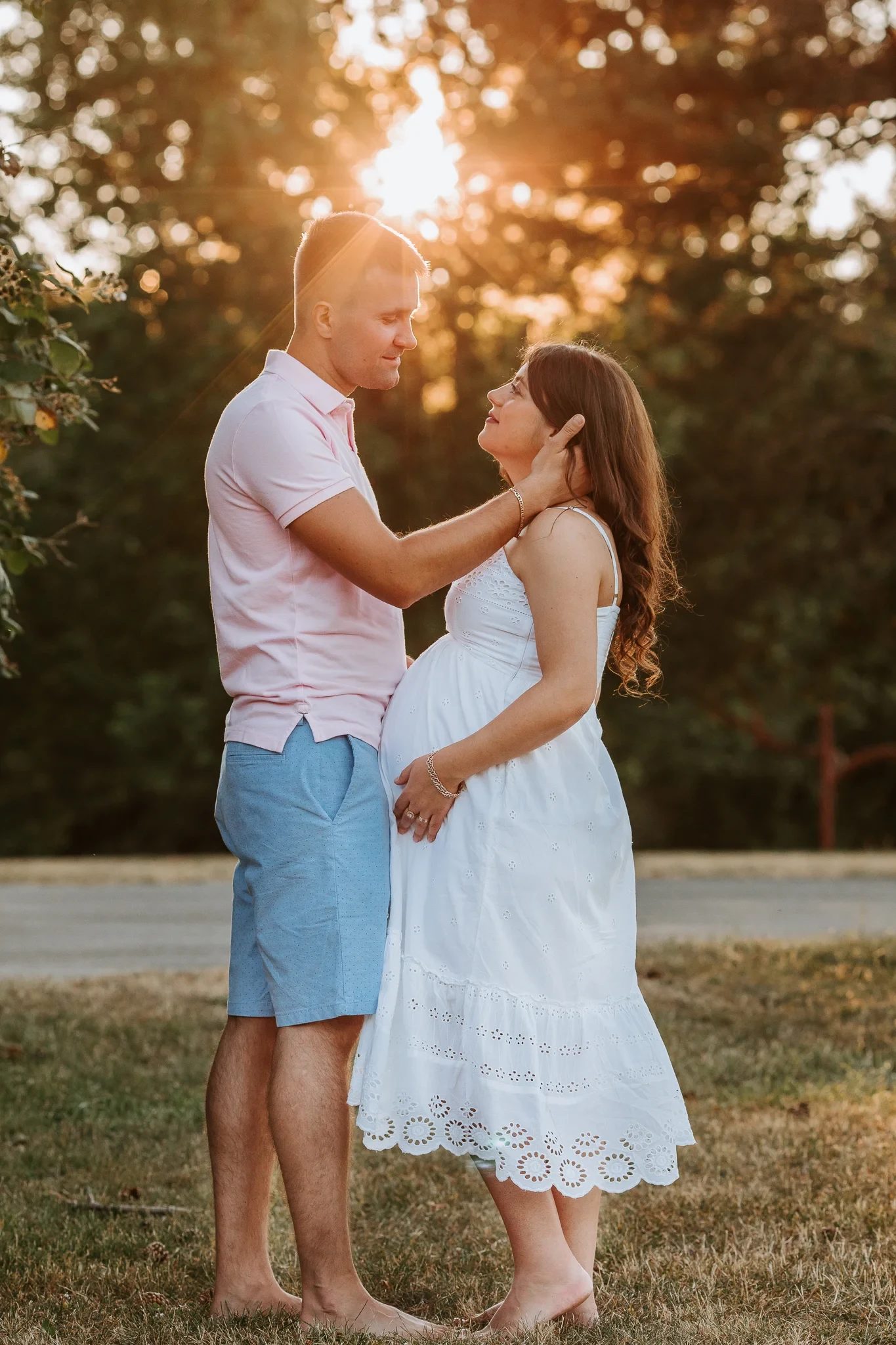Two adults embrace beneath glowing trees at sunset