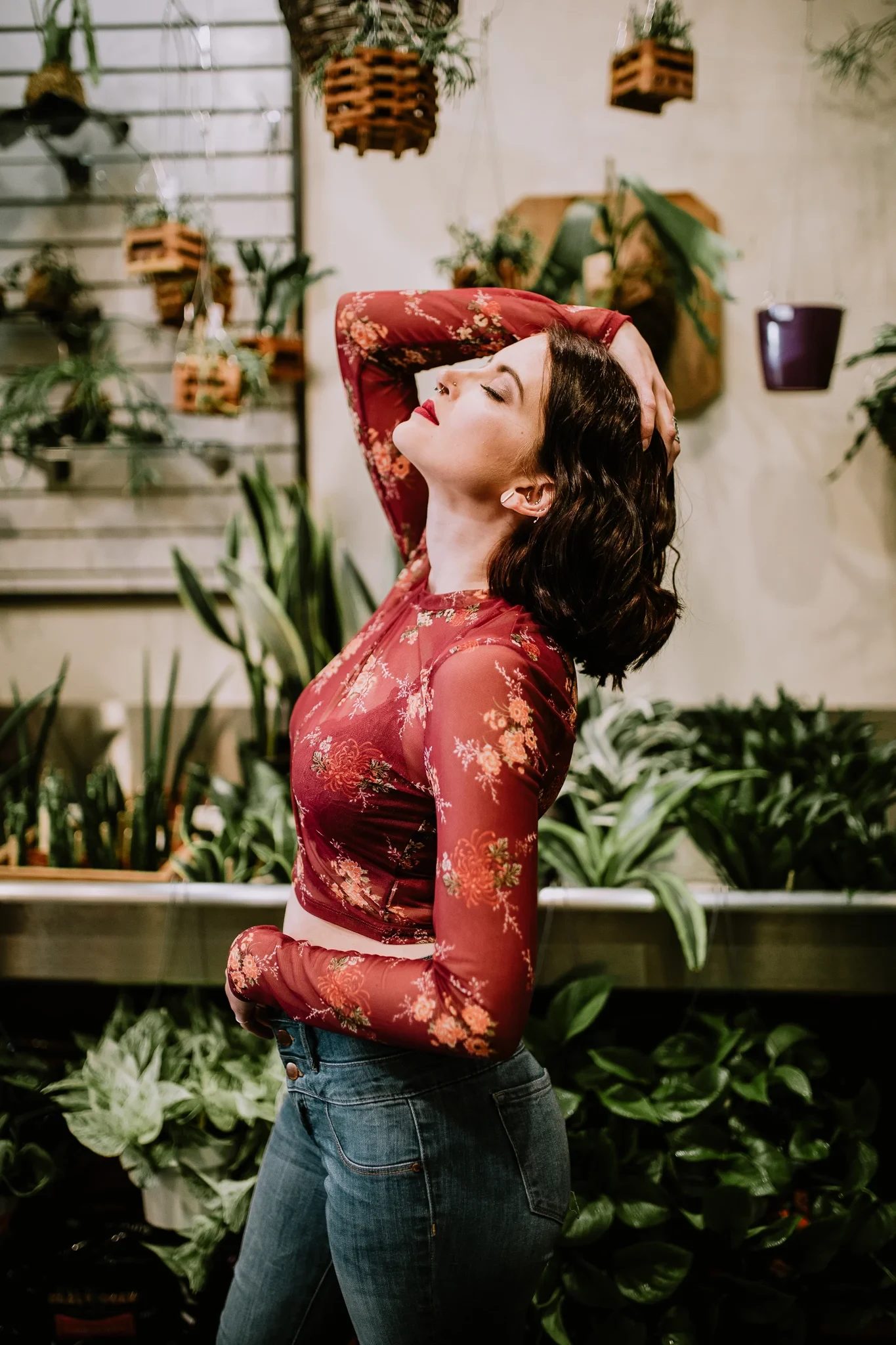 Woman in a red lace top poses among indoor plants