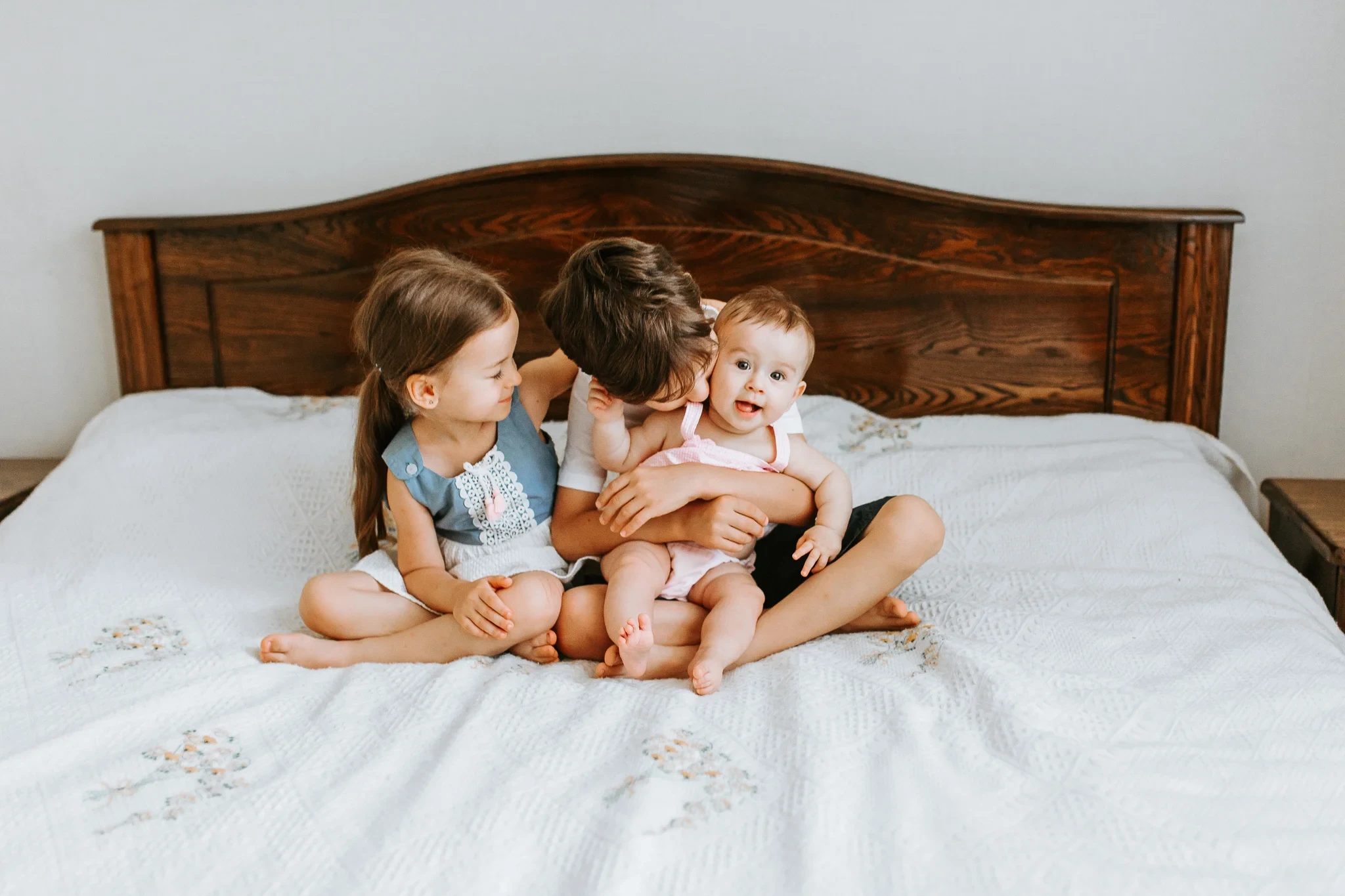 Three children cuddle together on a white bed