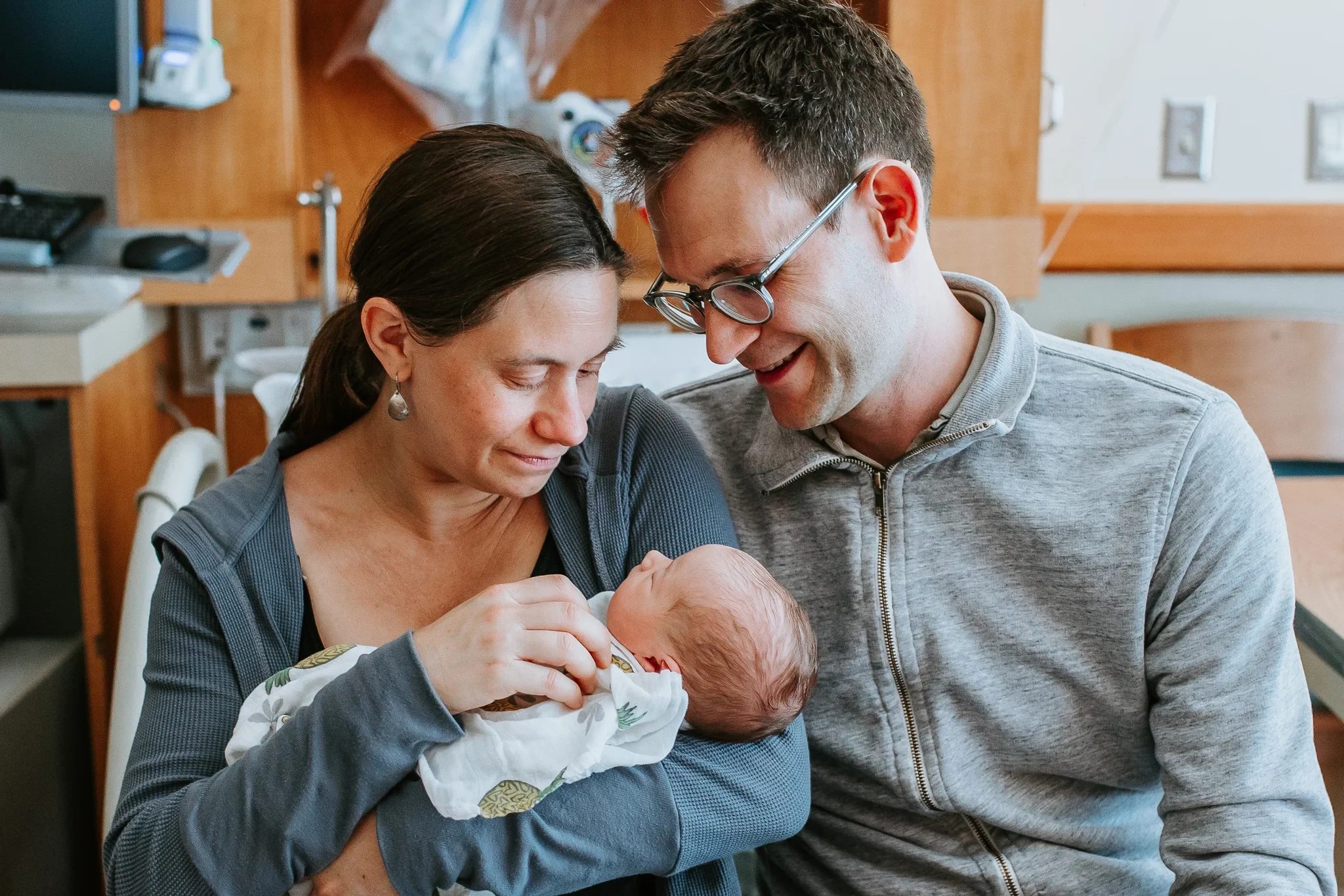 Two adults smile at the baby they are holding in a hospital room