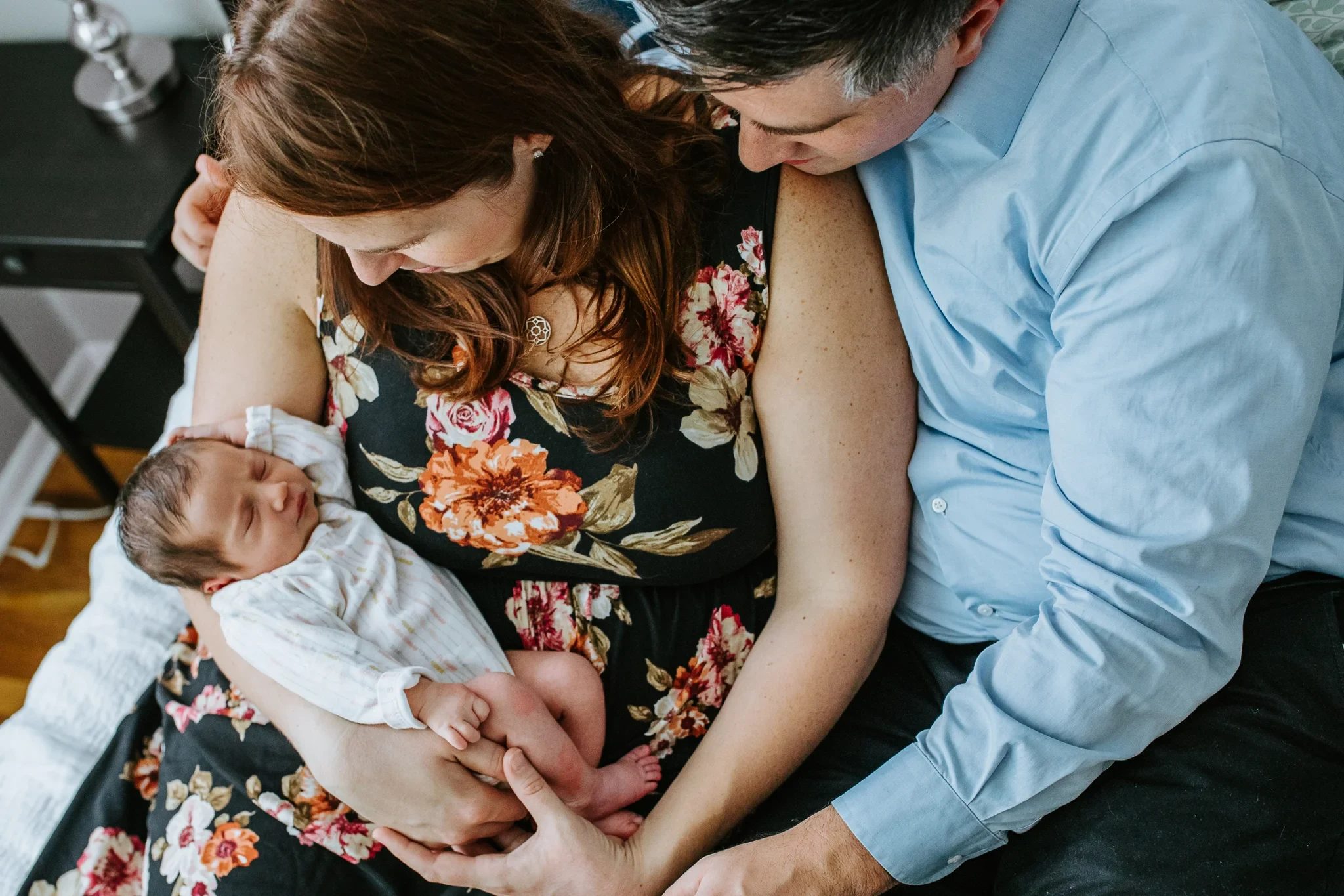 Two adults look down at a baby wrapped in white