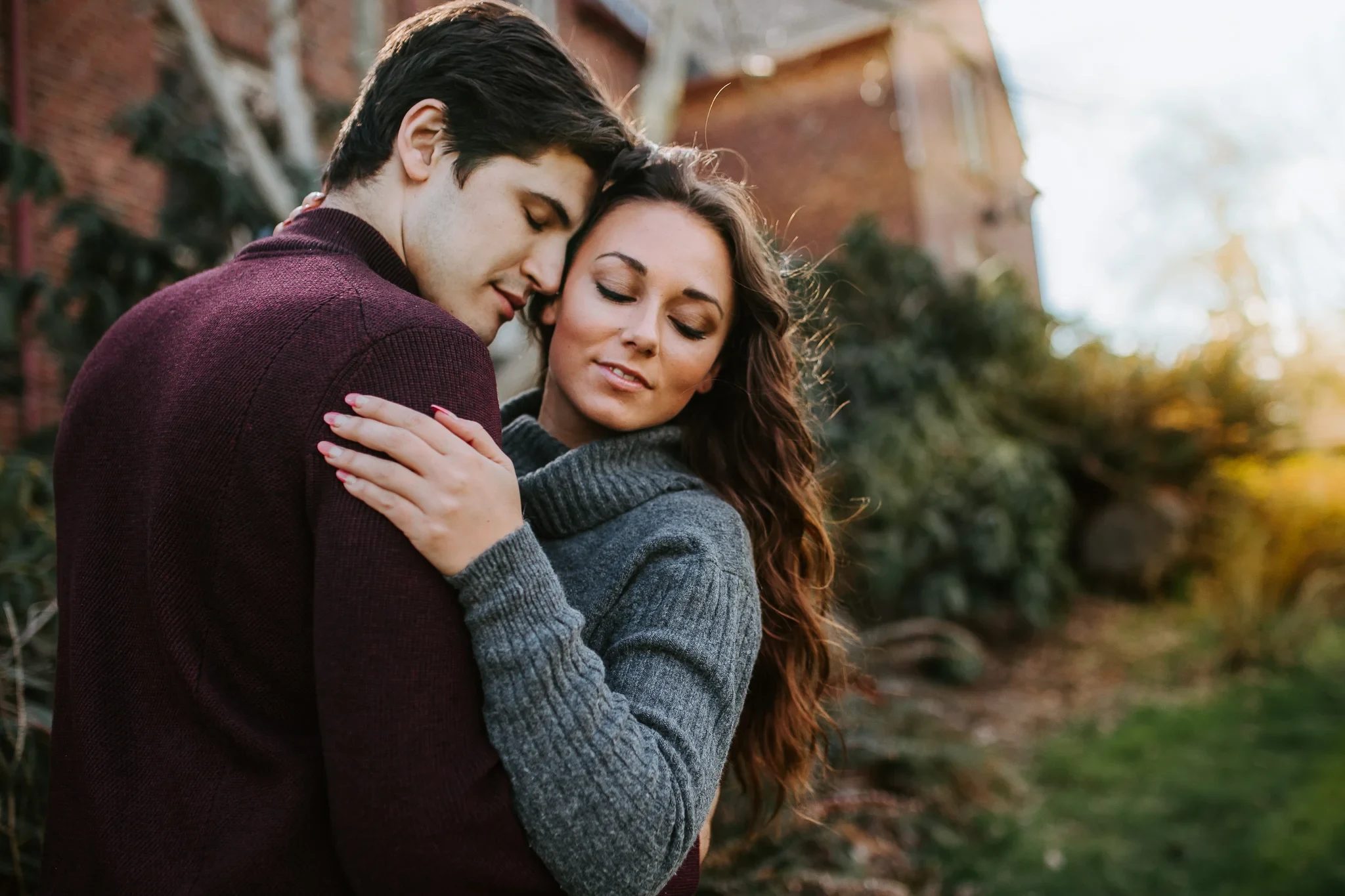 Two adults close their eyes while holding one another beside autumn foliage