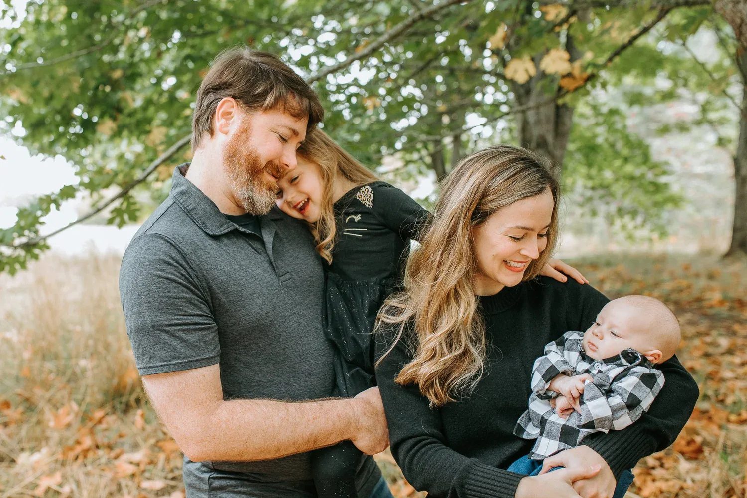 Two adults lean toward a baby held between them outdoors