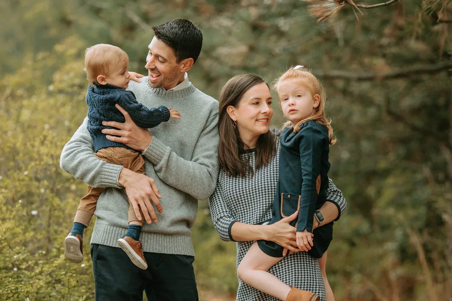 Two adults hold two children beneath autumn trees