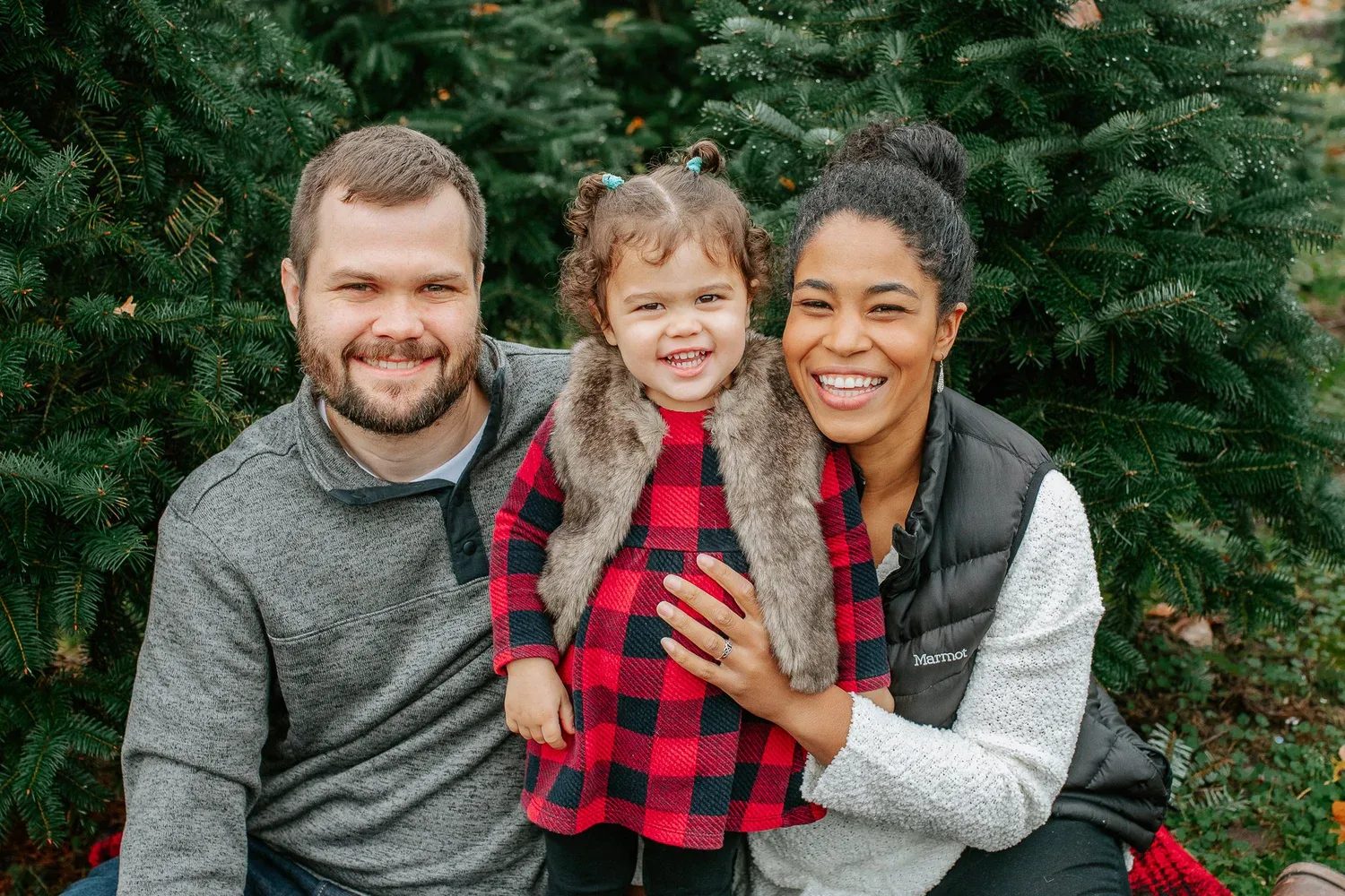 Two adults crouch beside a smiling child in red plaid
