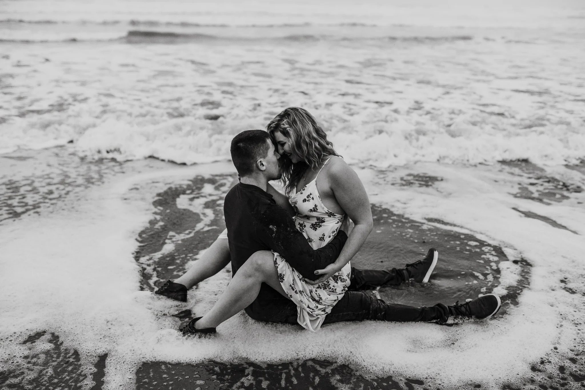 Black-and-white photograph of two adults seated on a rock surrounded by surf