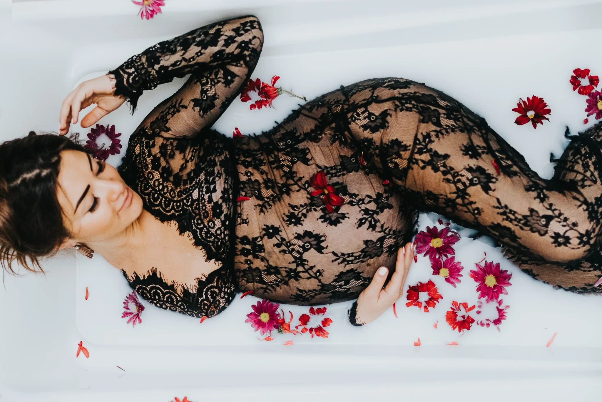 Woman in black floral lace reclines in white water scattered with red flowers