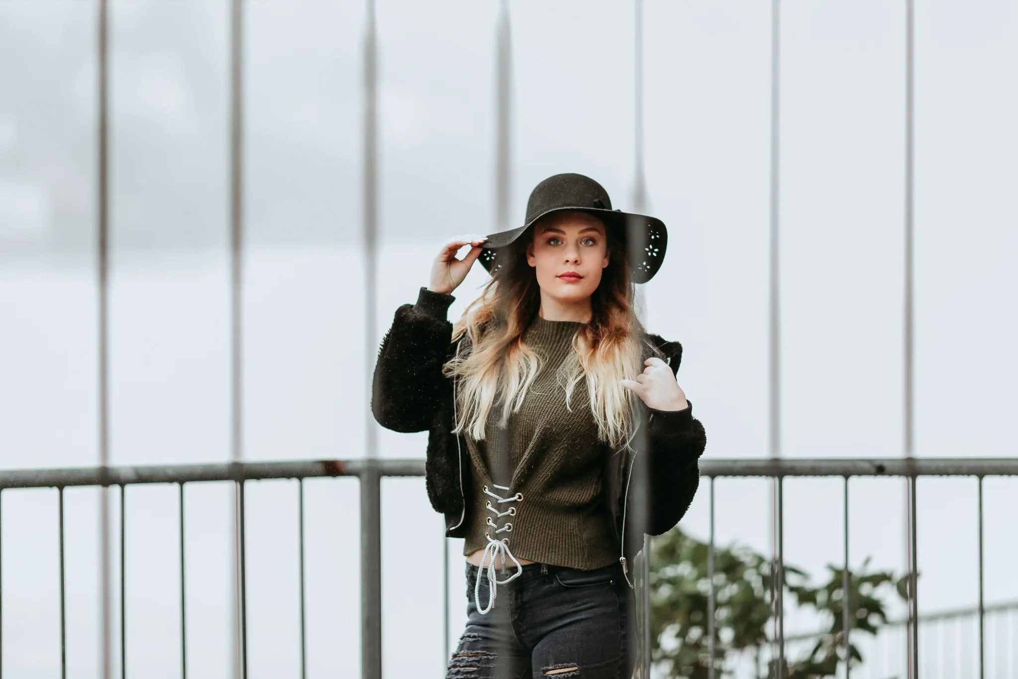 Woman in a wide black hat stands beside a metal railing