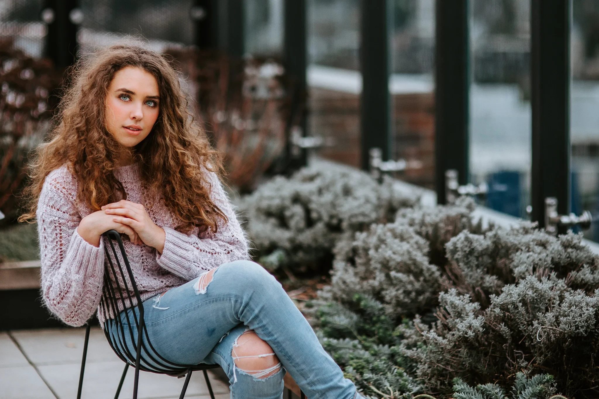 Woman with curly hair sits in a chair beside rooftop greenery