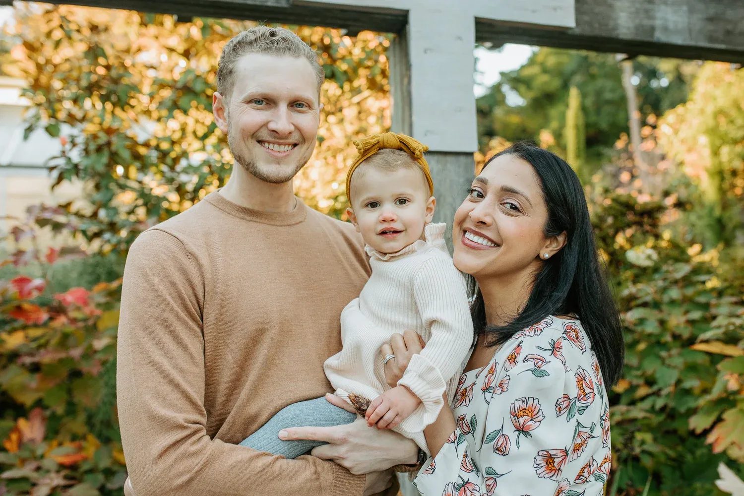 Two adults smile with a toddler wearing a yellow bow