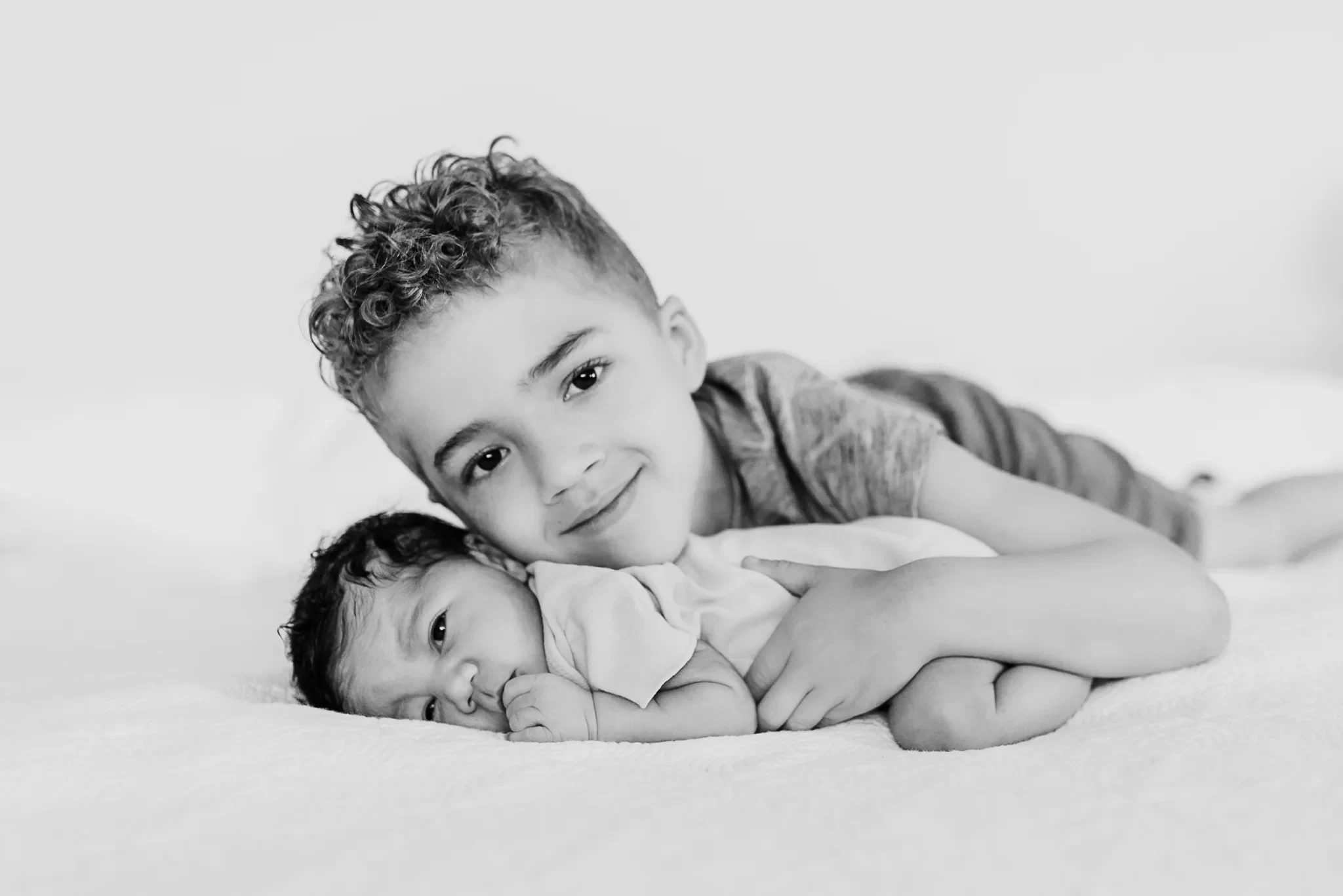 Black-and-white portrait of a child cuddling a baby on a bed