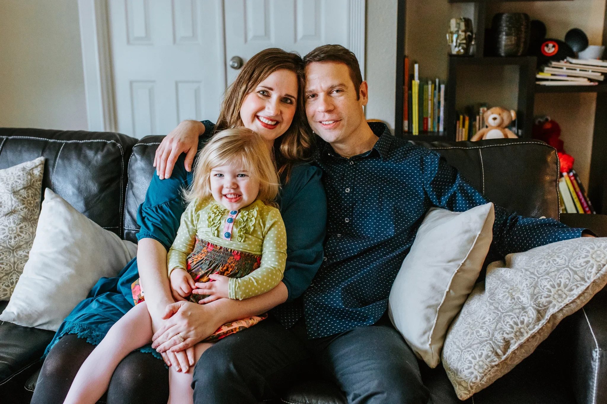 Two adults and a child sit close together on a dark sofa