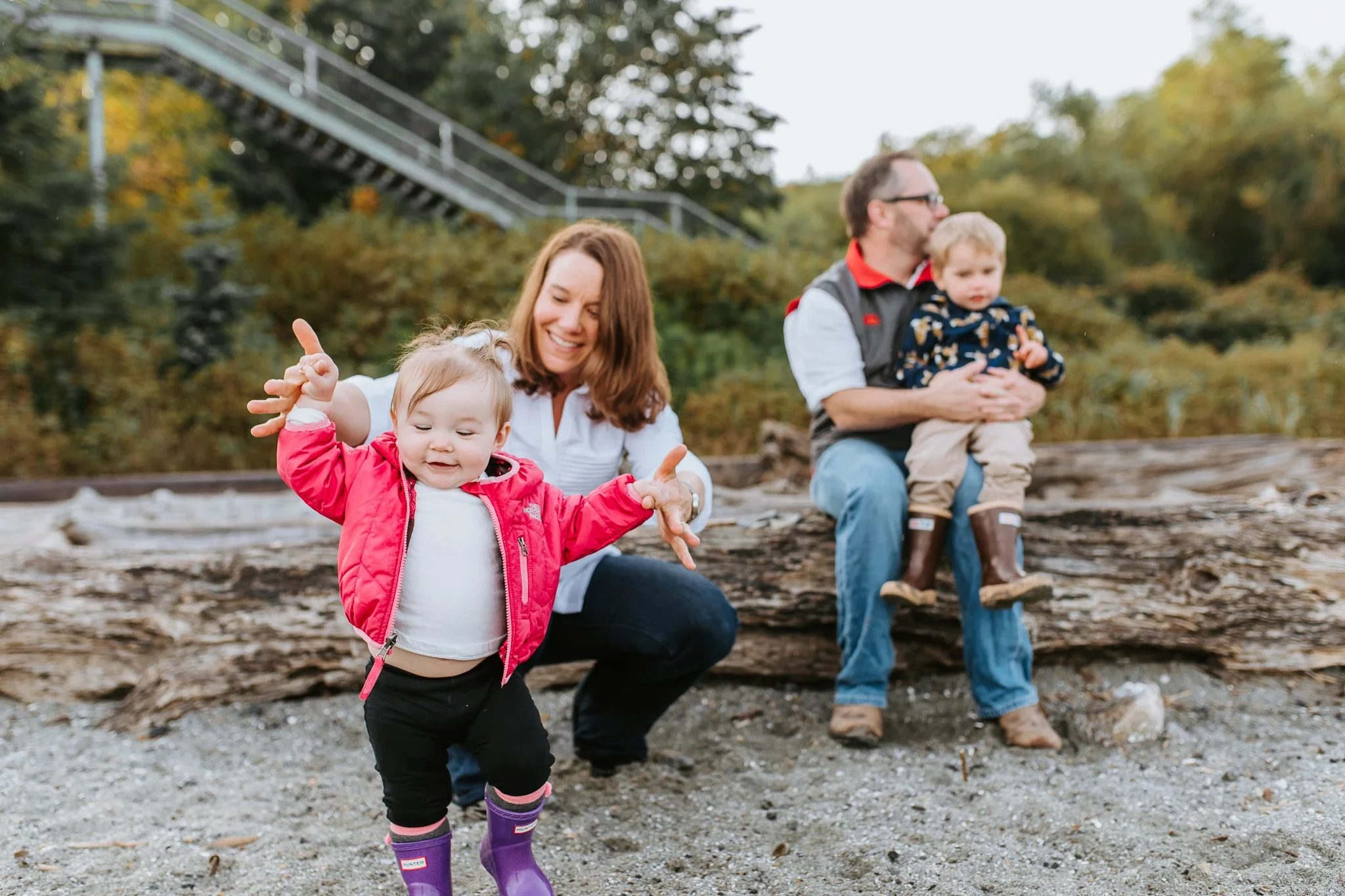 Child in a pink jacket reaches toward the camera beside seated family members