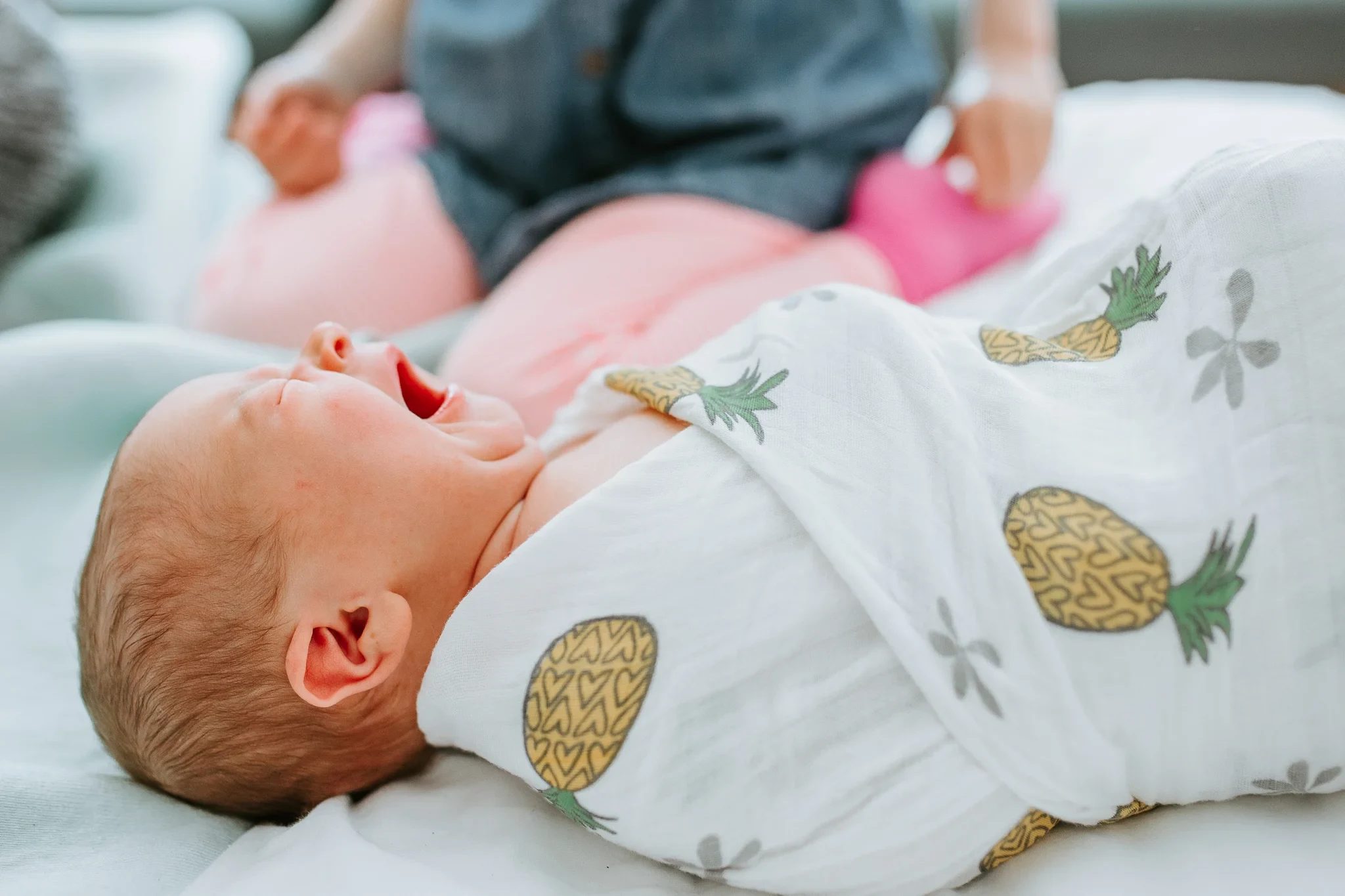 Baby yawns while lying in a pineapple-print wrap