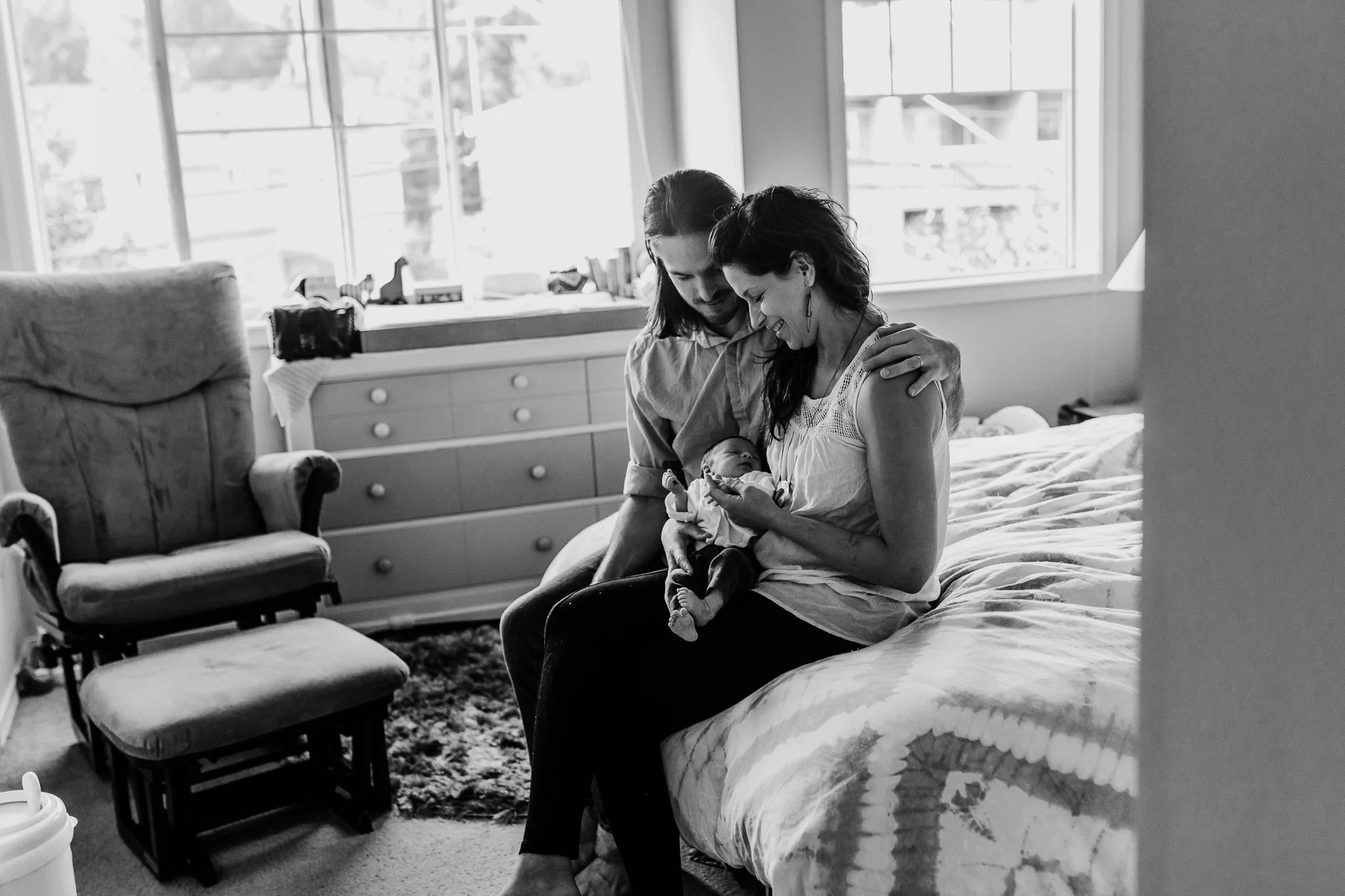 Black-and-white photograph of two adults holding a baby beside a bedroom window