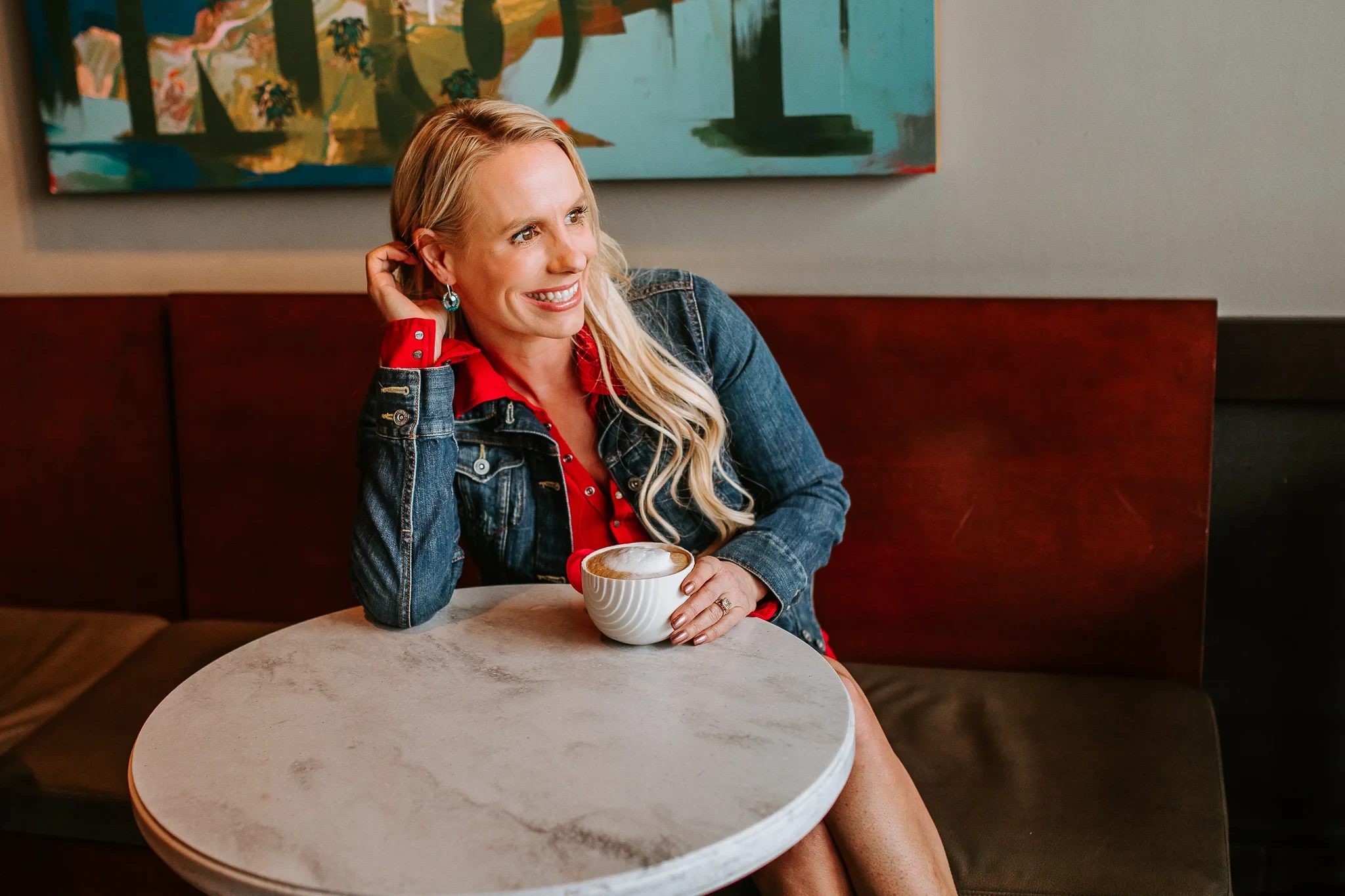 Woman smiles while holding a cup at a small café table