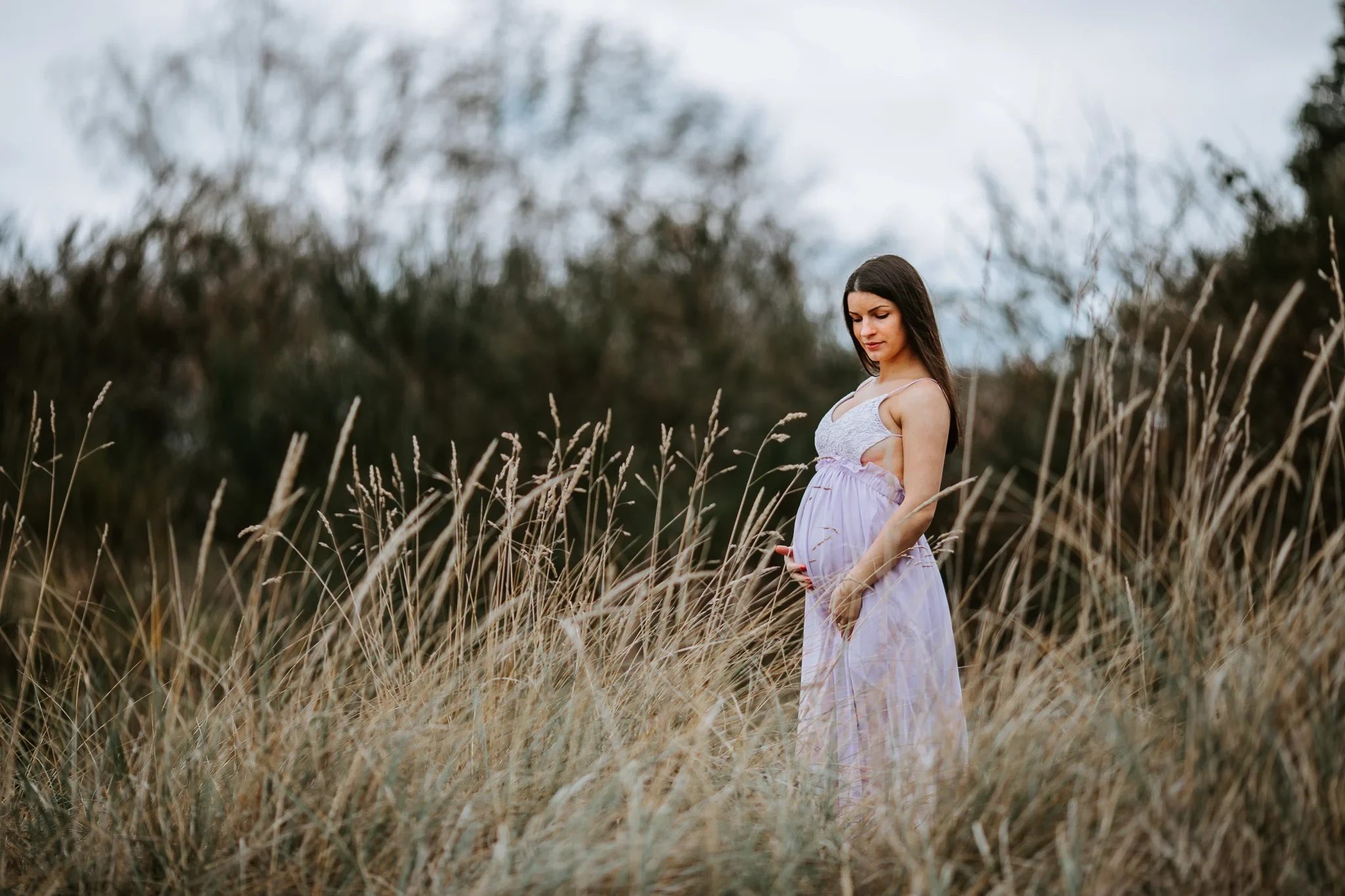 Woman in a pale pink dress stands among tall dry grasses