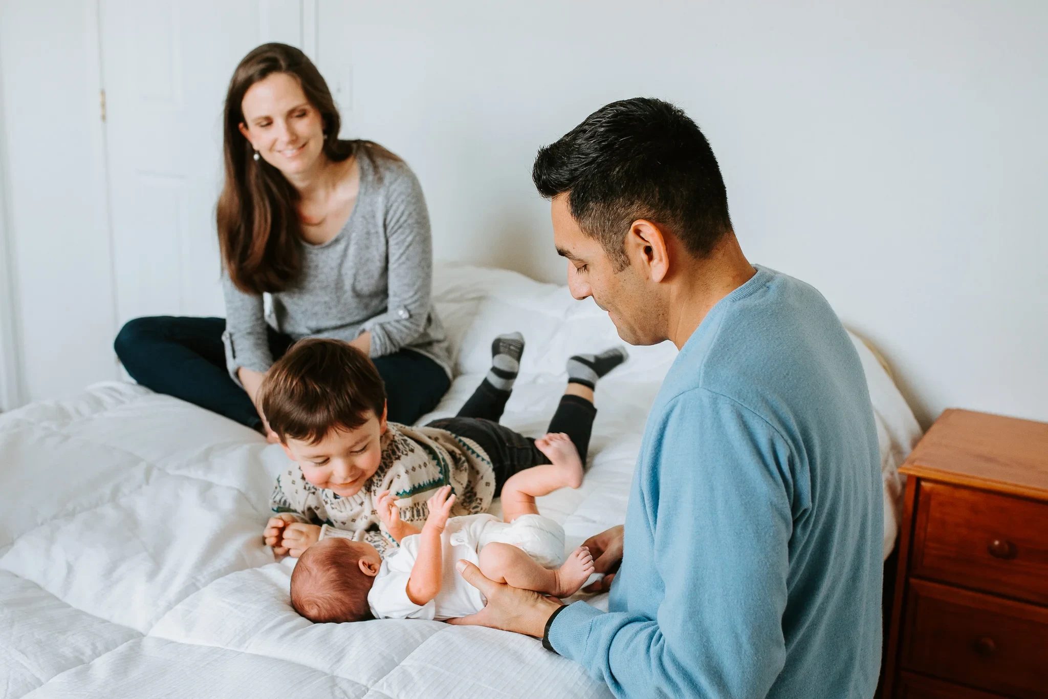 Family leans over a baby lying on white bedding