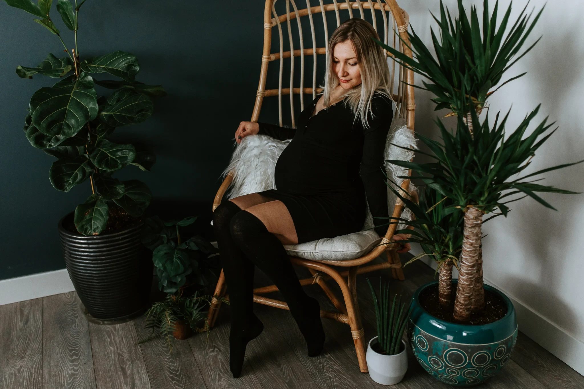 Woman dressed in black sits in a wicker chair surrounded by houseplants