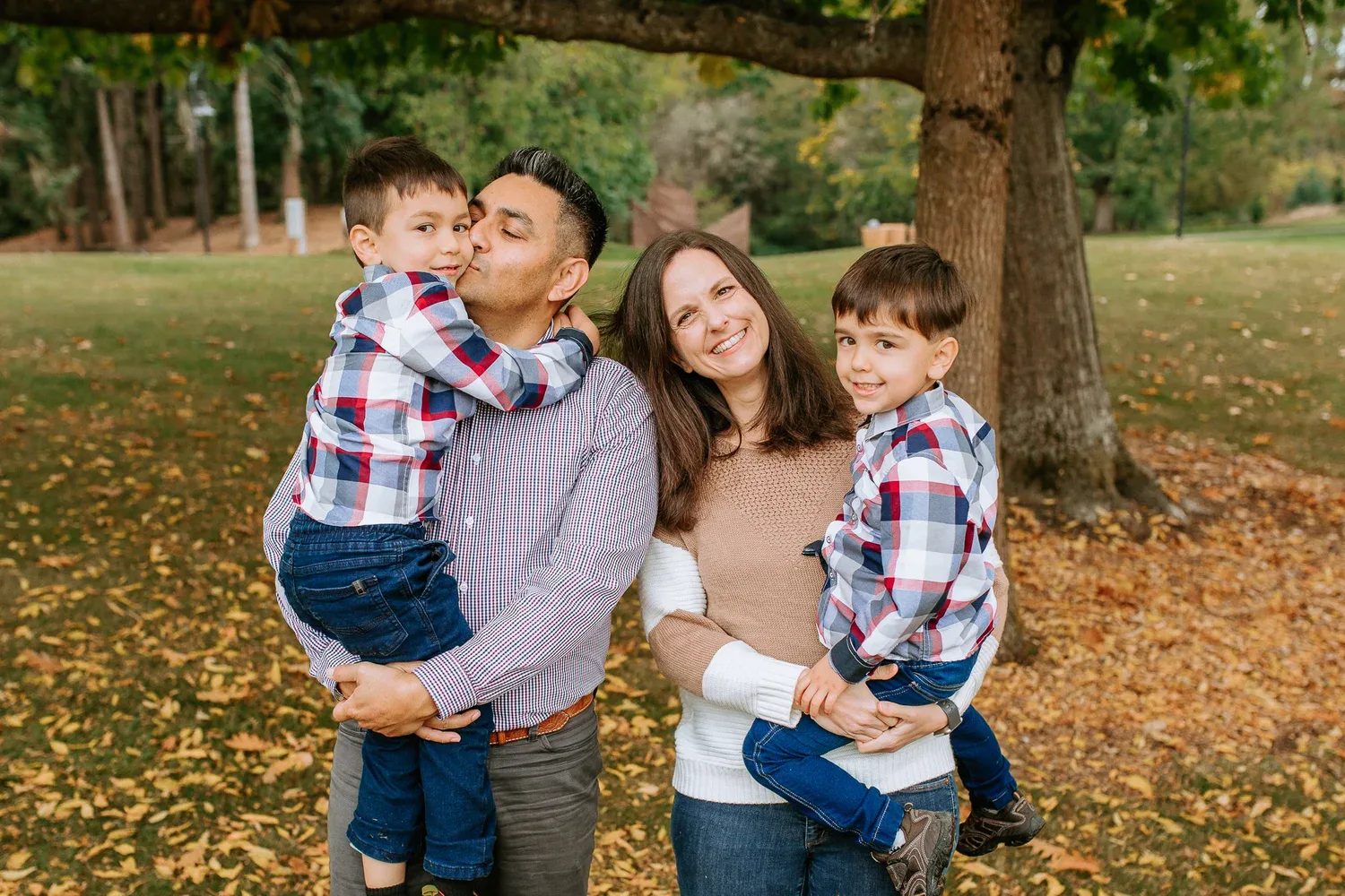 Two adults hold two children in checked shirts beneath a tree