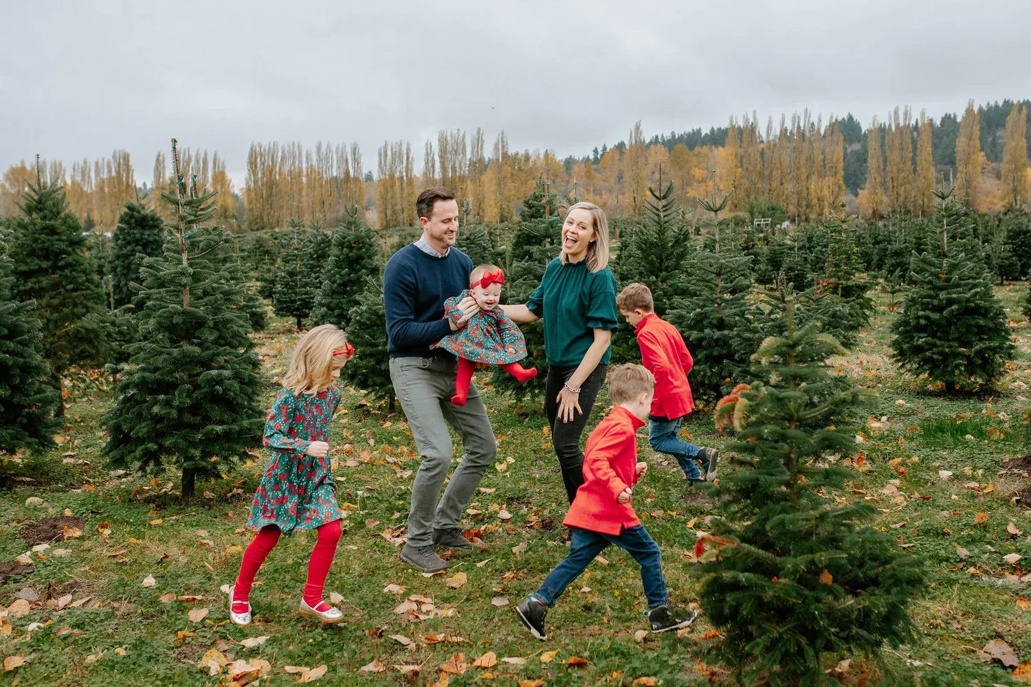 Children run in a circle around two adults at a tree farm