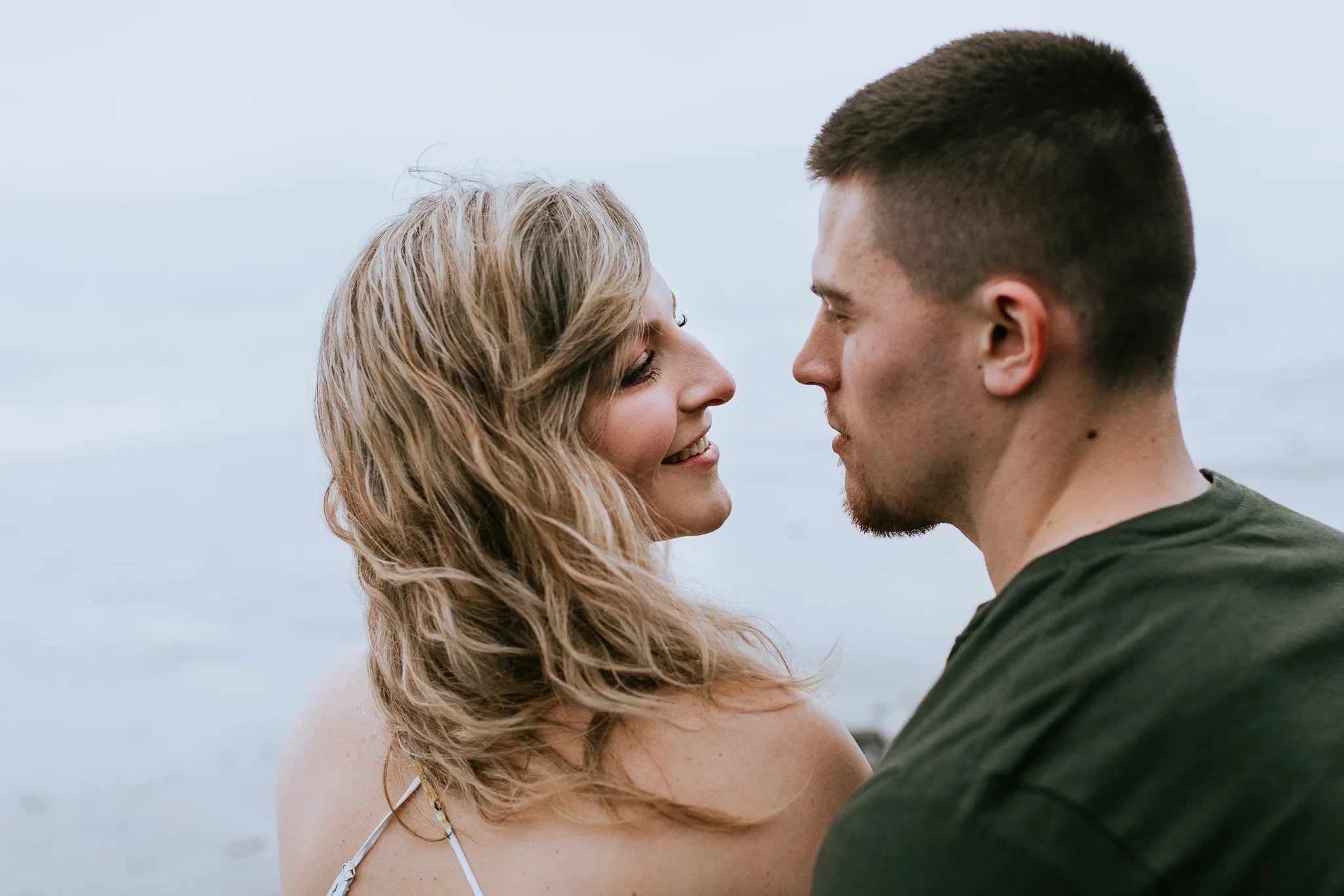 Two adults gaze at one another beside calm water