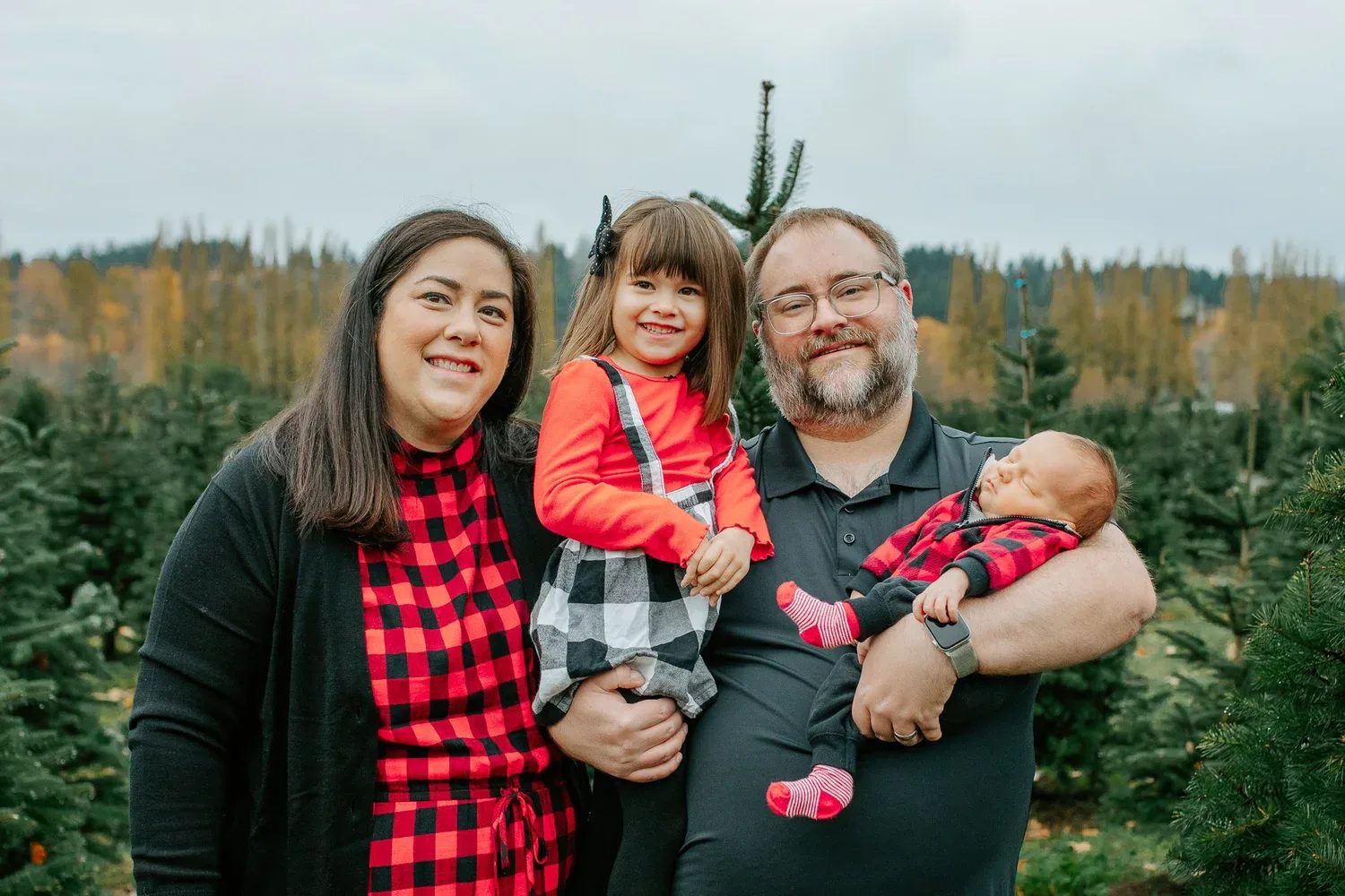 Two adults hold a child and baby at a tree farm