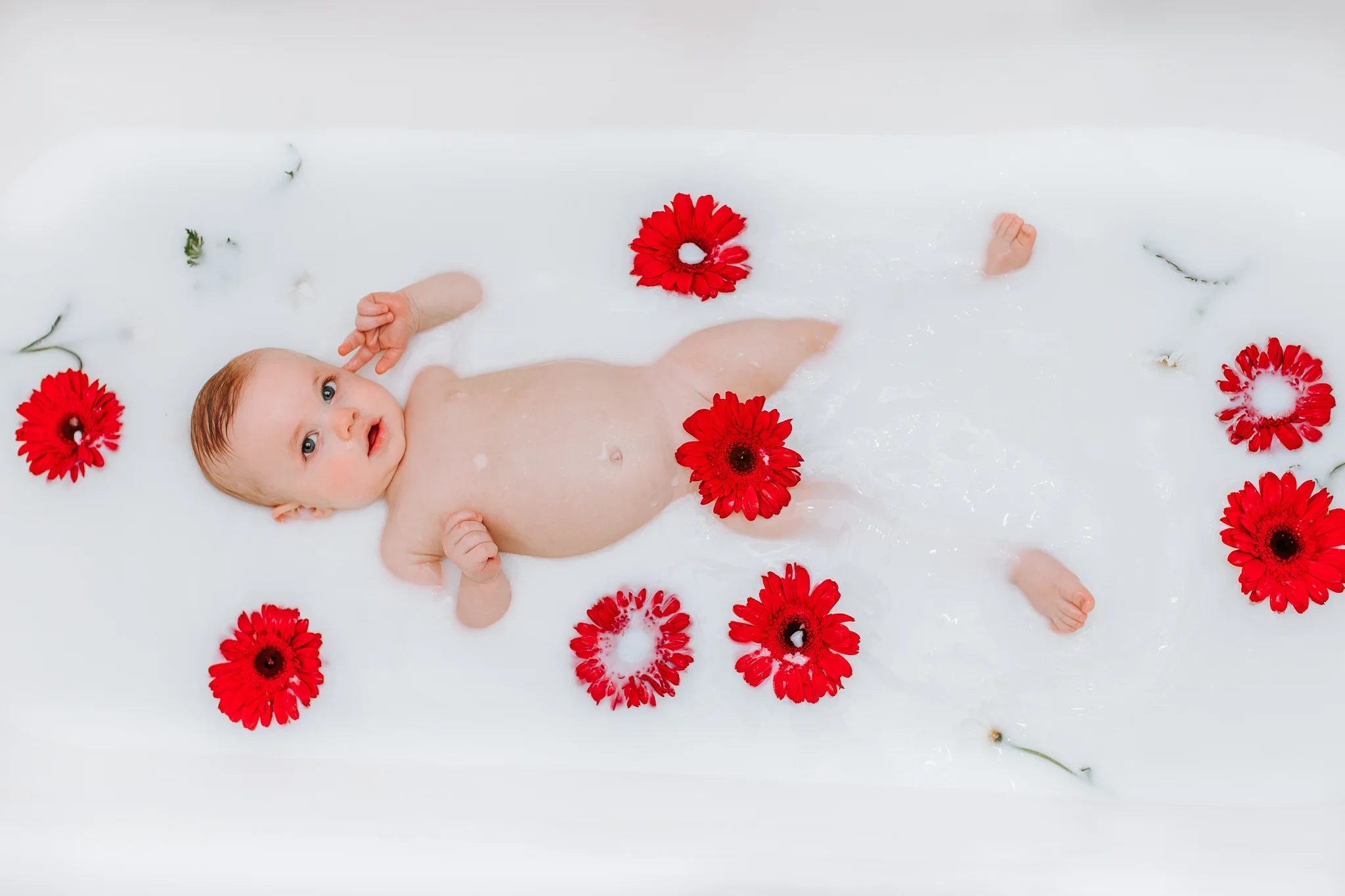 Baby lies on white fabric surrounded by red flowers