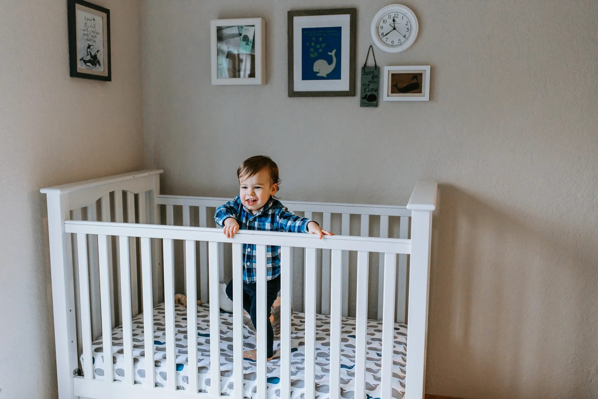 Small child stands holding the rail of a white crib