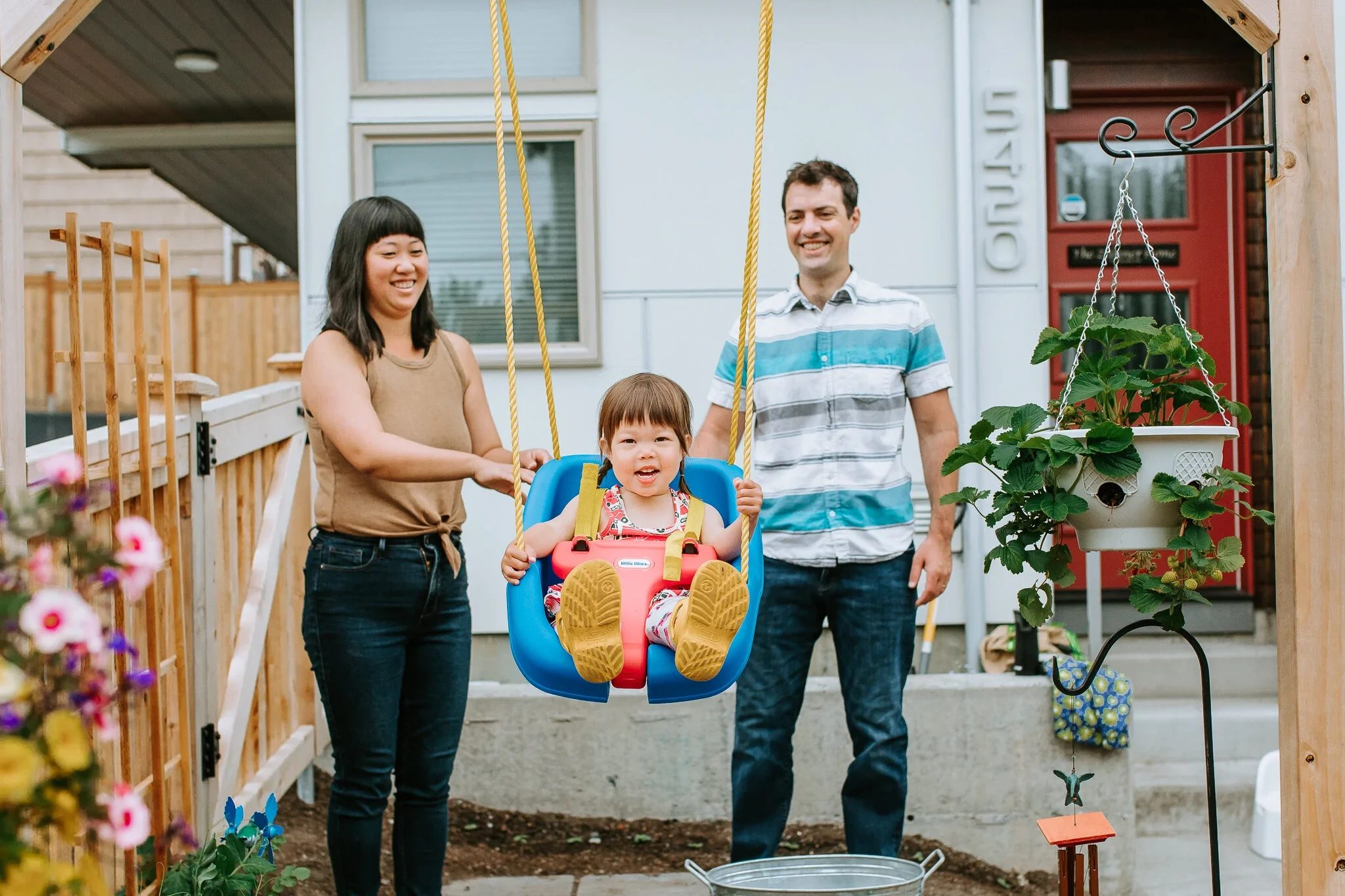Two adults stand beside a smiling child in a porch swing