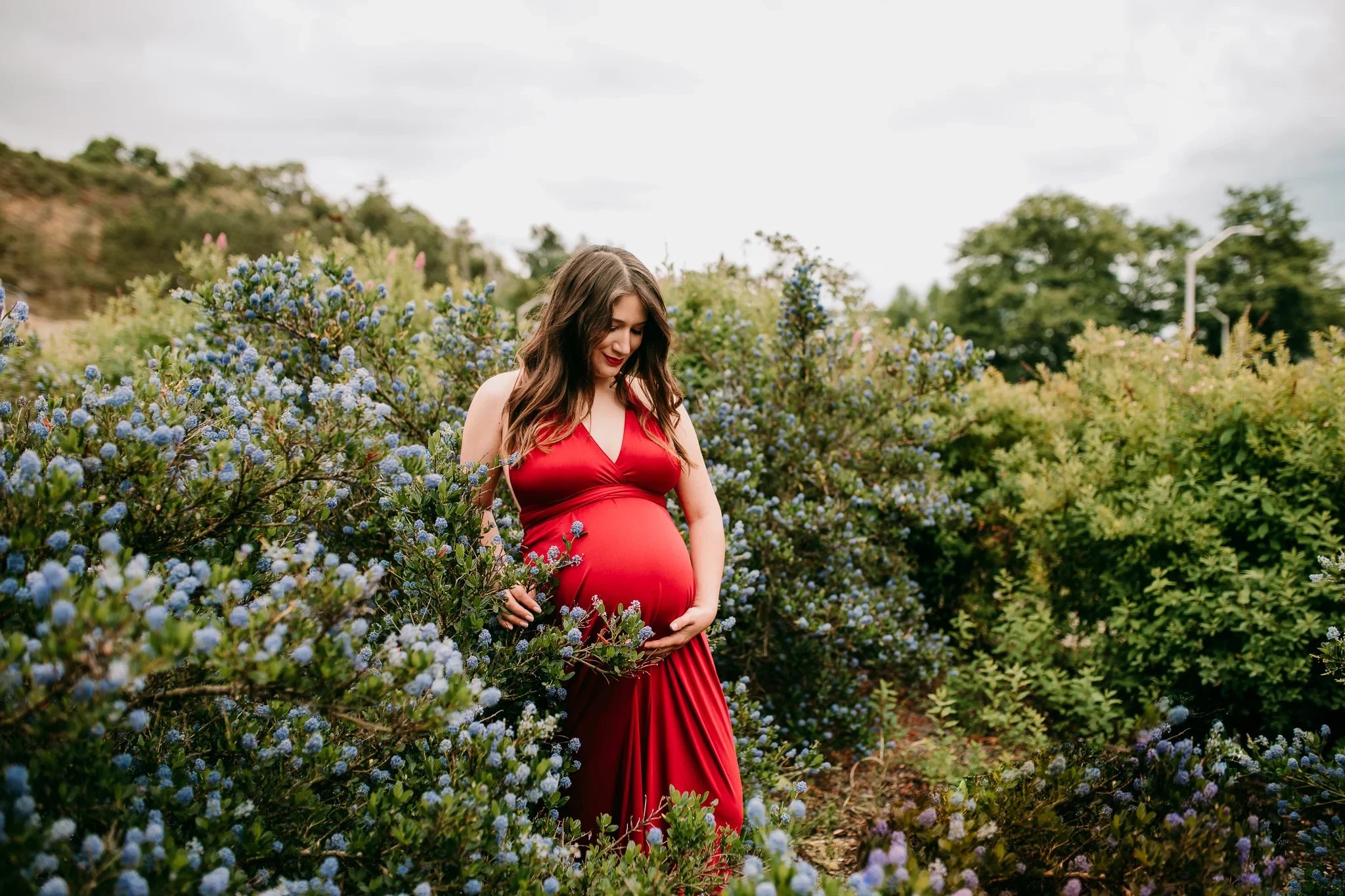 Woman in a red dress stands among flowering shrubs