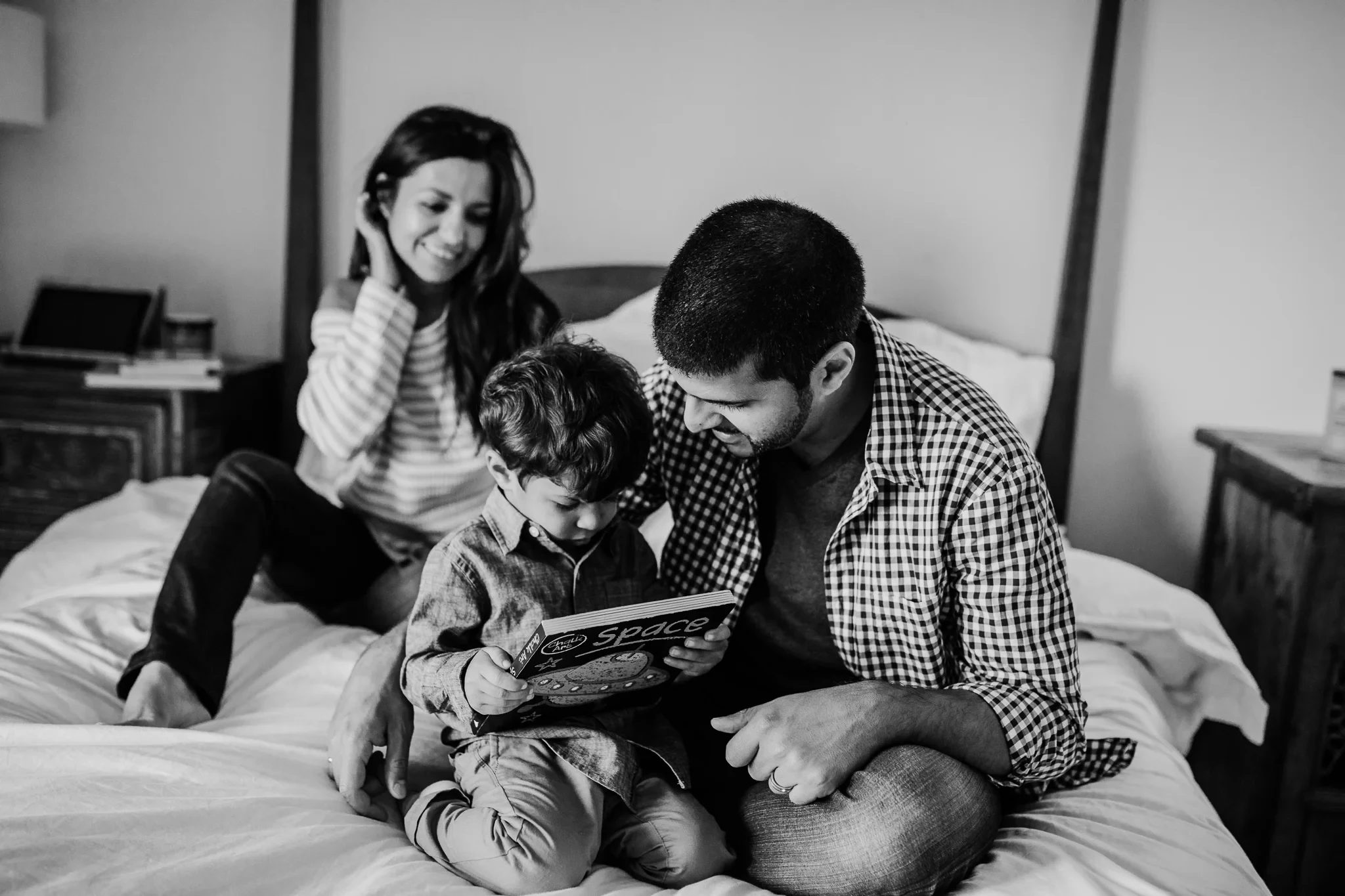 Black-and-white photograph of a family sharing a picture book on a bed