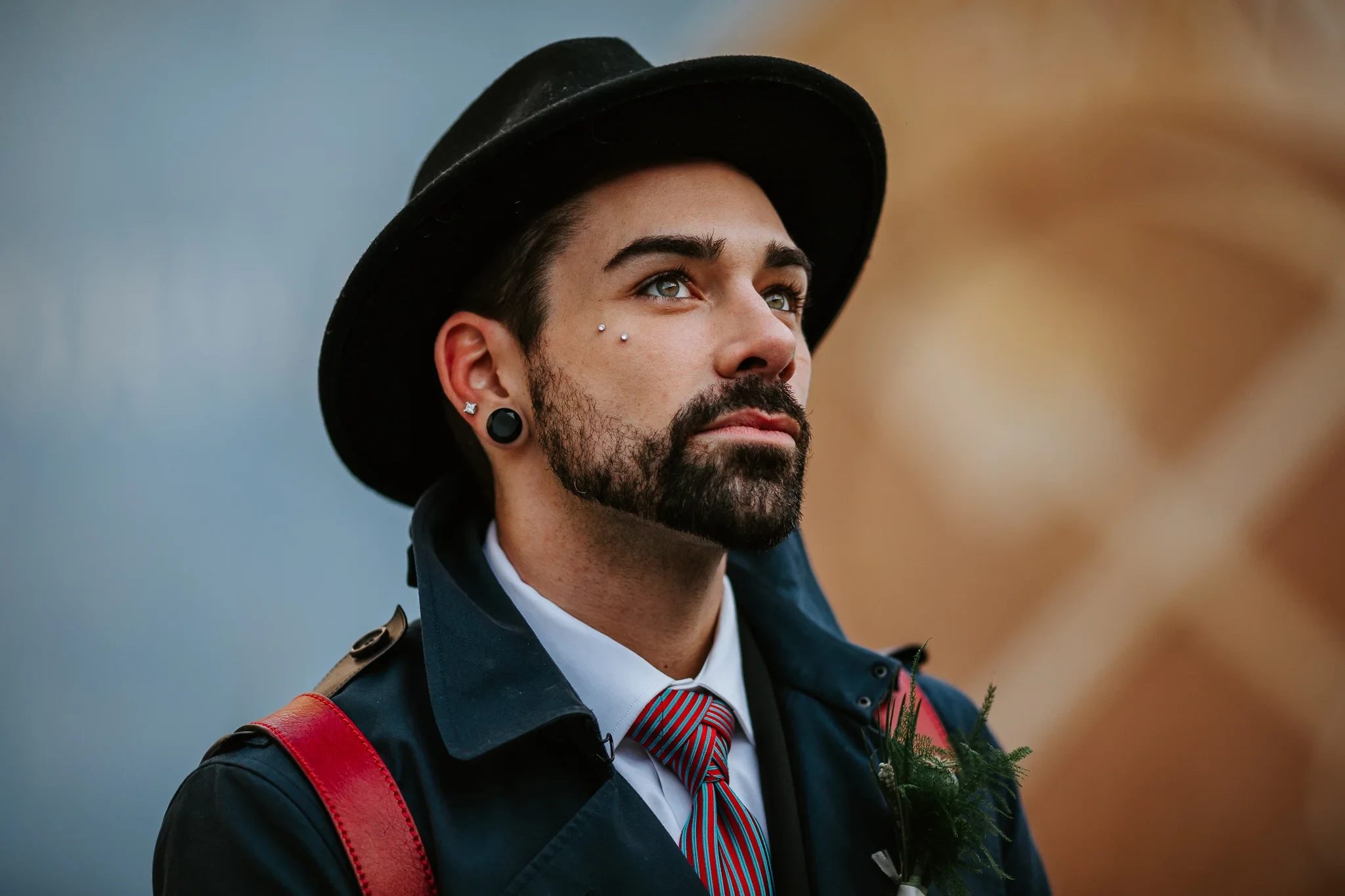Man wearing a black hat and tie looks upward