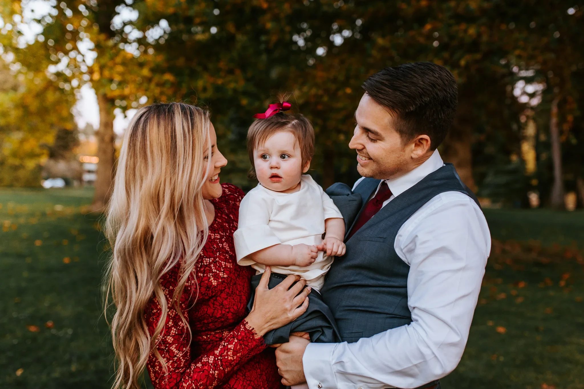 Two adults hold a child beneath golden autumn leaves
