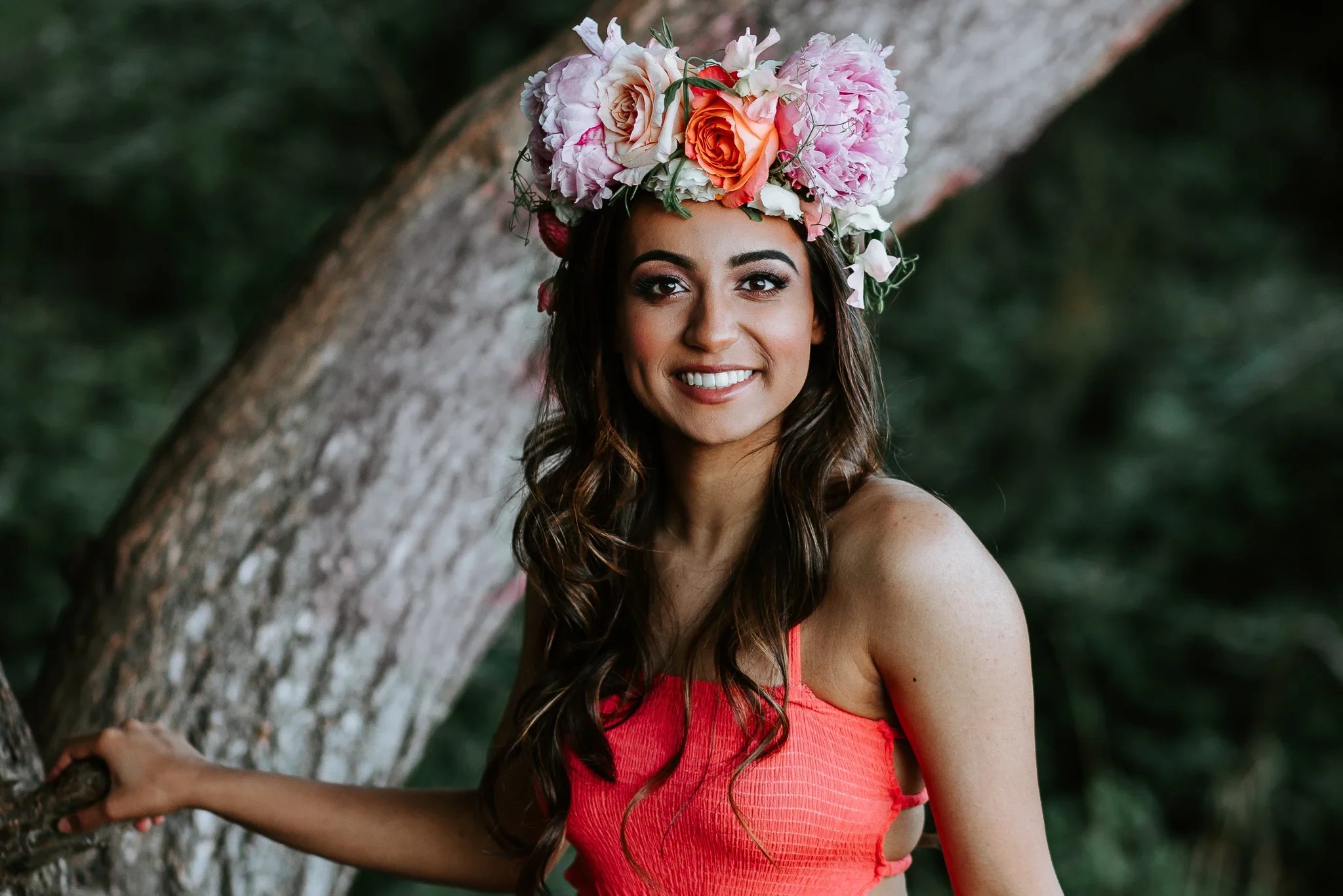Woman wearing a flower crown smiles beside a tree