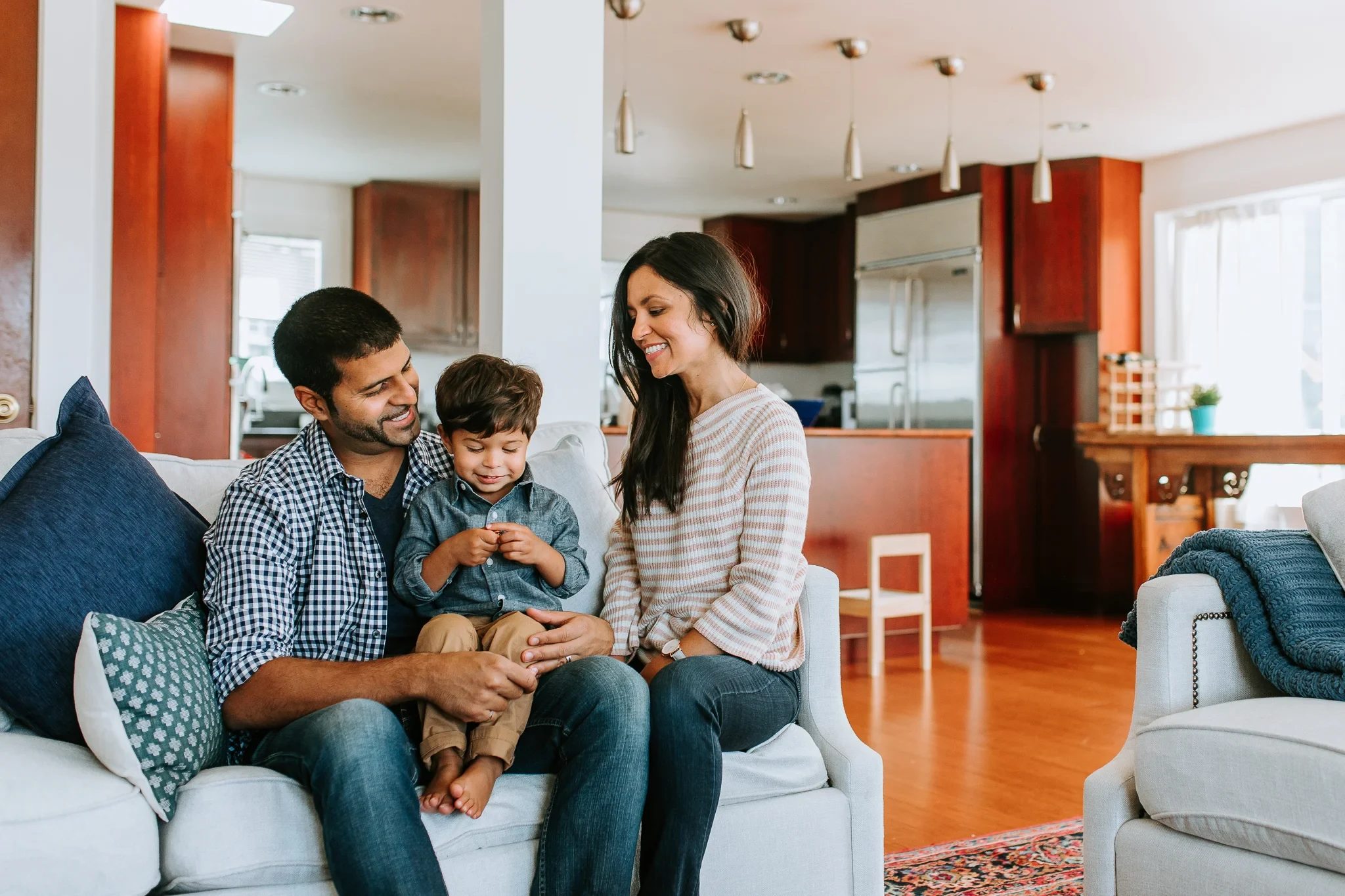 Two adults sit with a child on a sofa in a bright living room