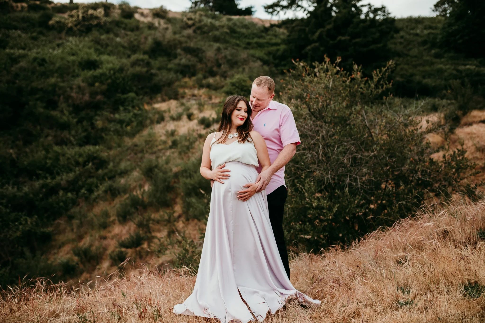 Two adults in pastel clothing stand together in a golden meadow