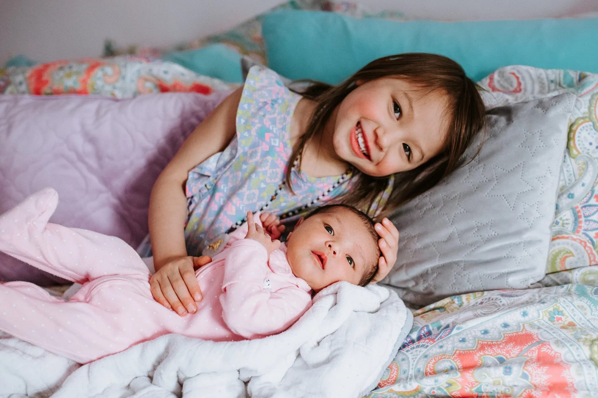 Child cuddles a baby on a bed with colorful pillows
