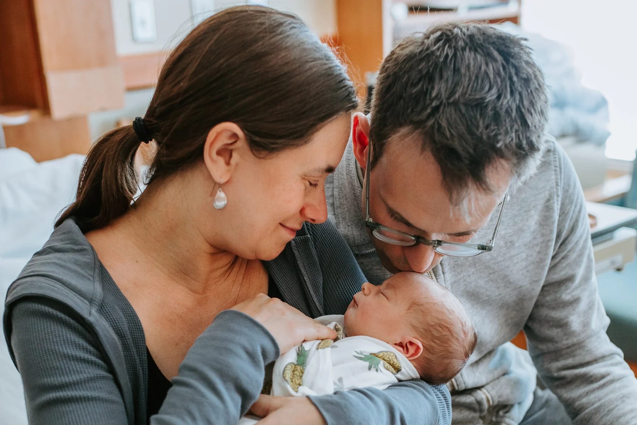 Two adults lean close above a sleeping baby in their arms