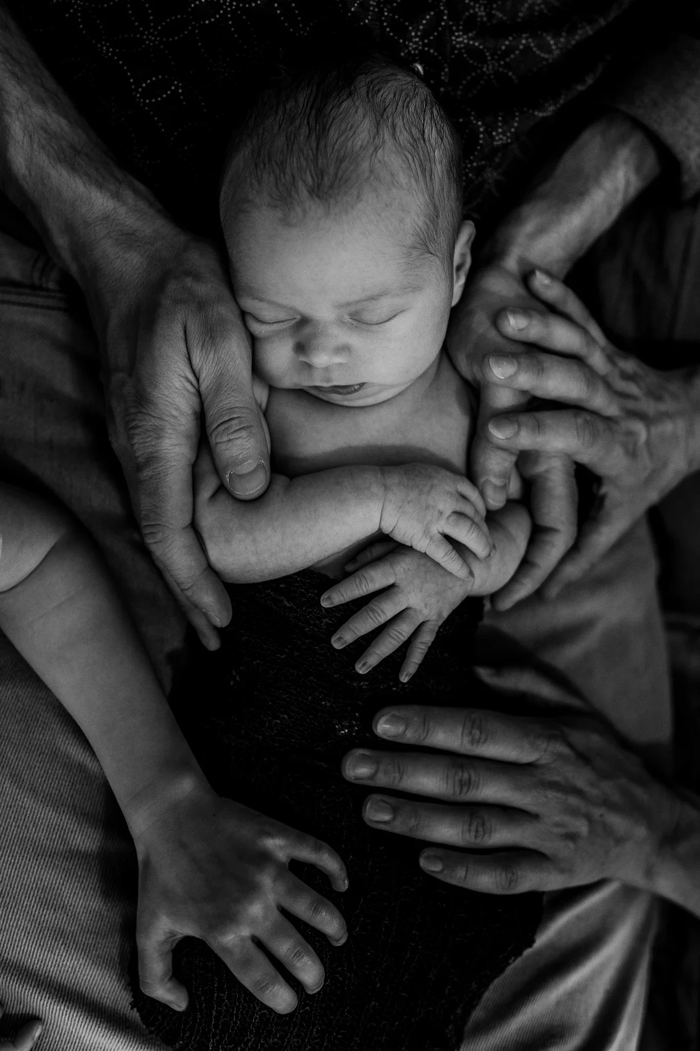 Black-and-white photograph of several hands gently surrounding a sleeping baby