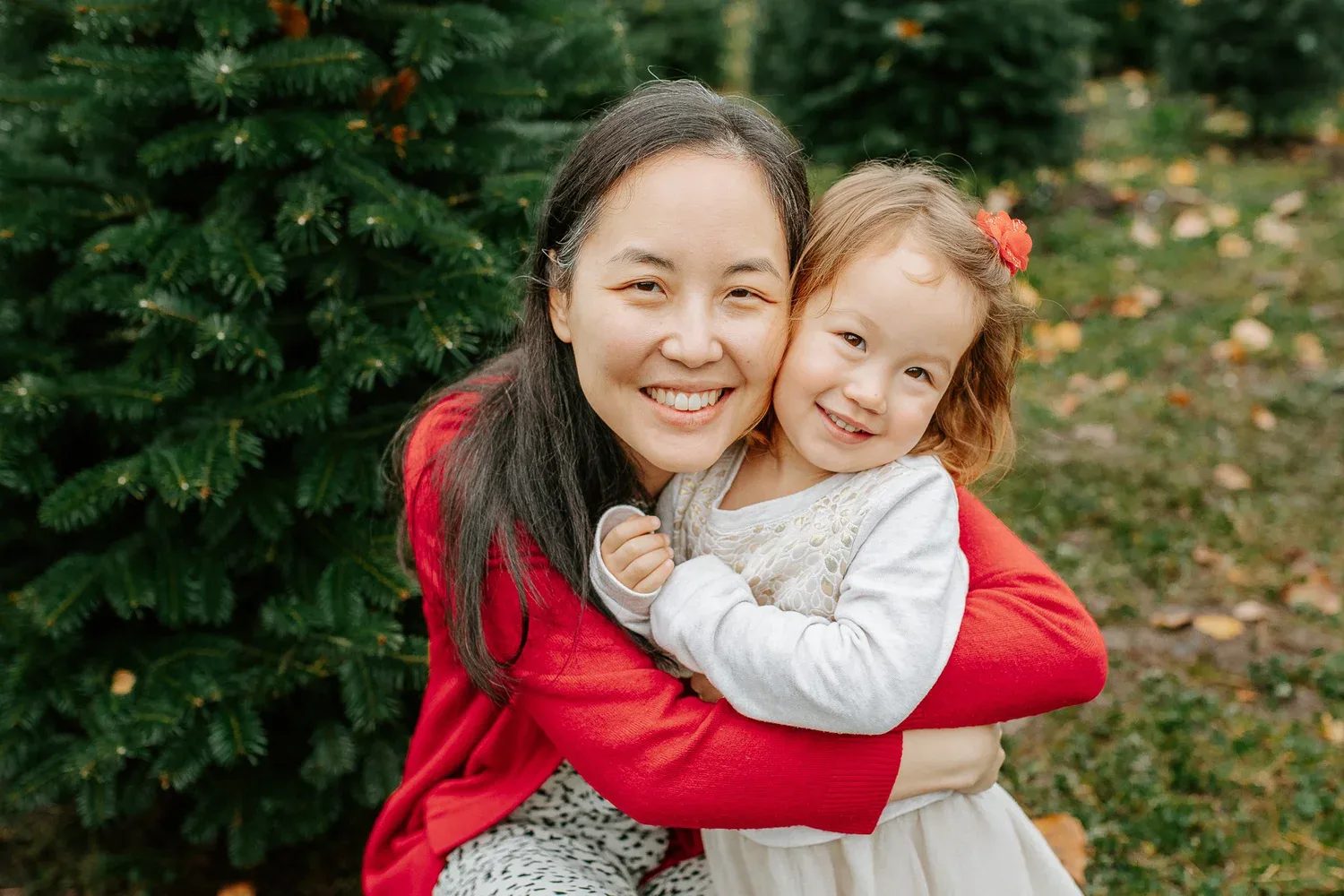 Woman and child in red clothing cuddle beneath an evergreen tree