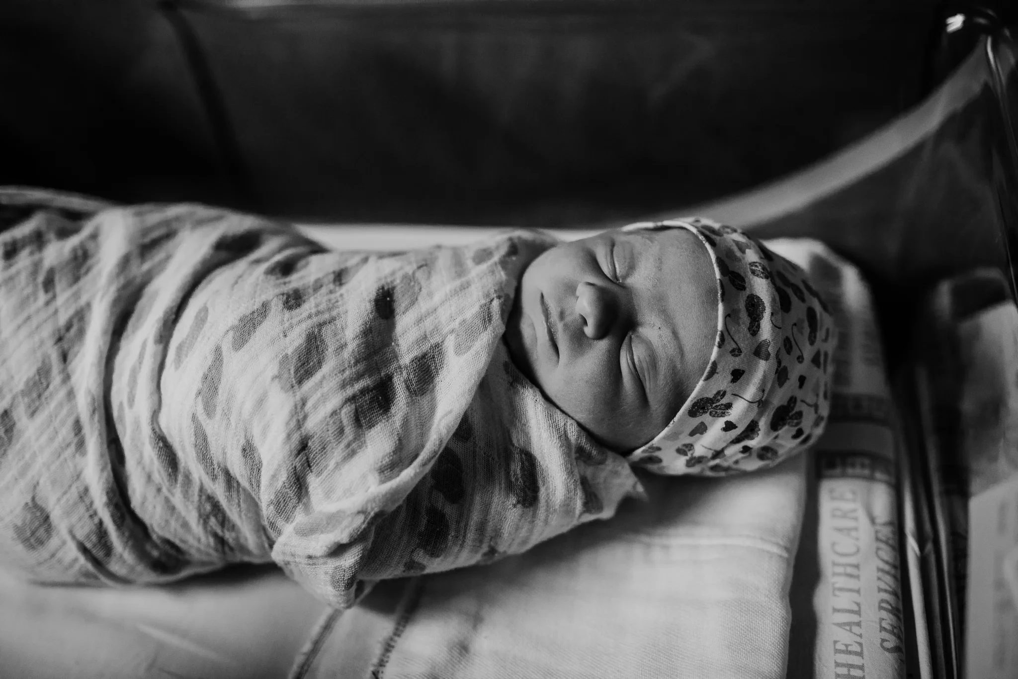 Black-and-white overhead photograph of a baby curled inside a patterned wrap