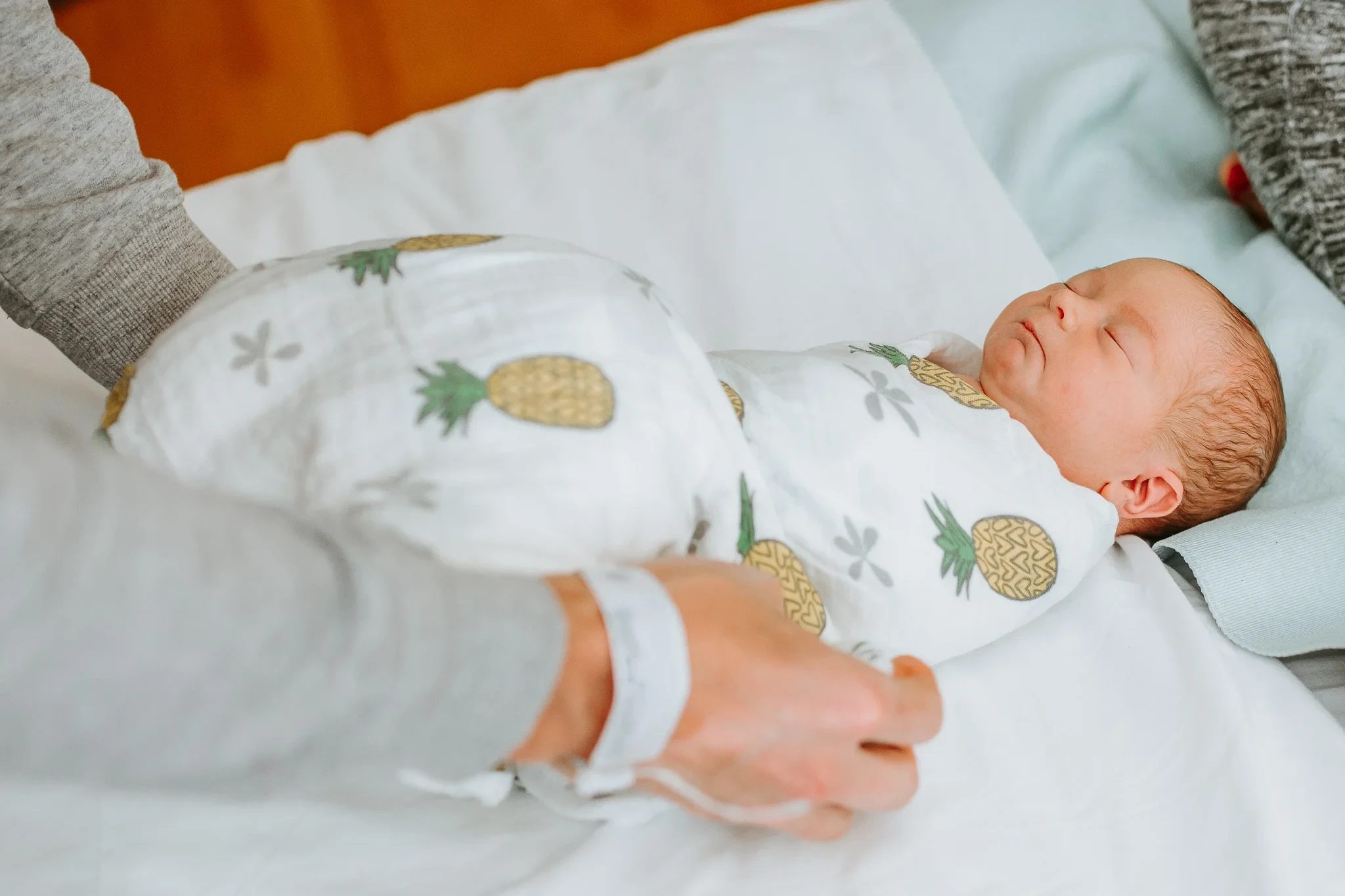 Baby in a pineapple-print wrap rests on a hospital bed