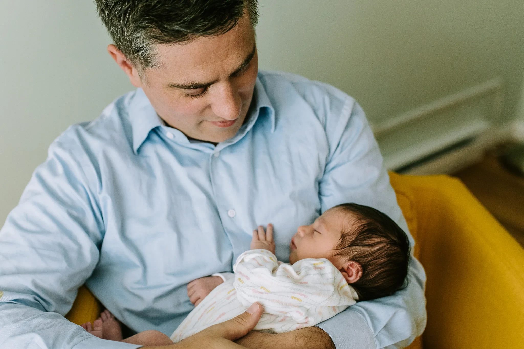 Man in a light blue shirt looks down at a baby in his arms