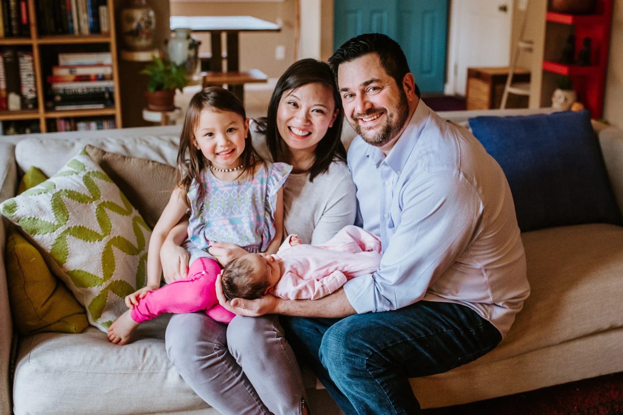 Two adults and a child smile together while holding a baby on a sofa