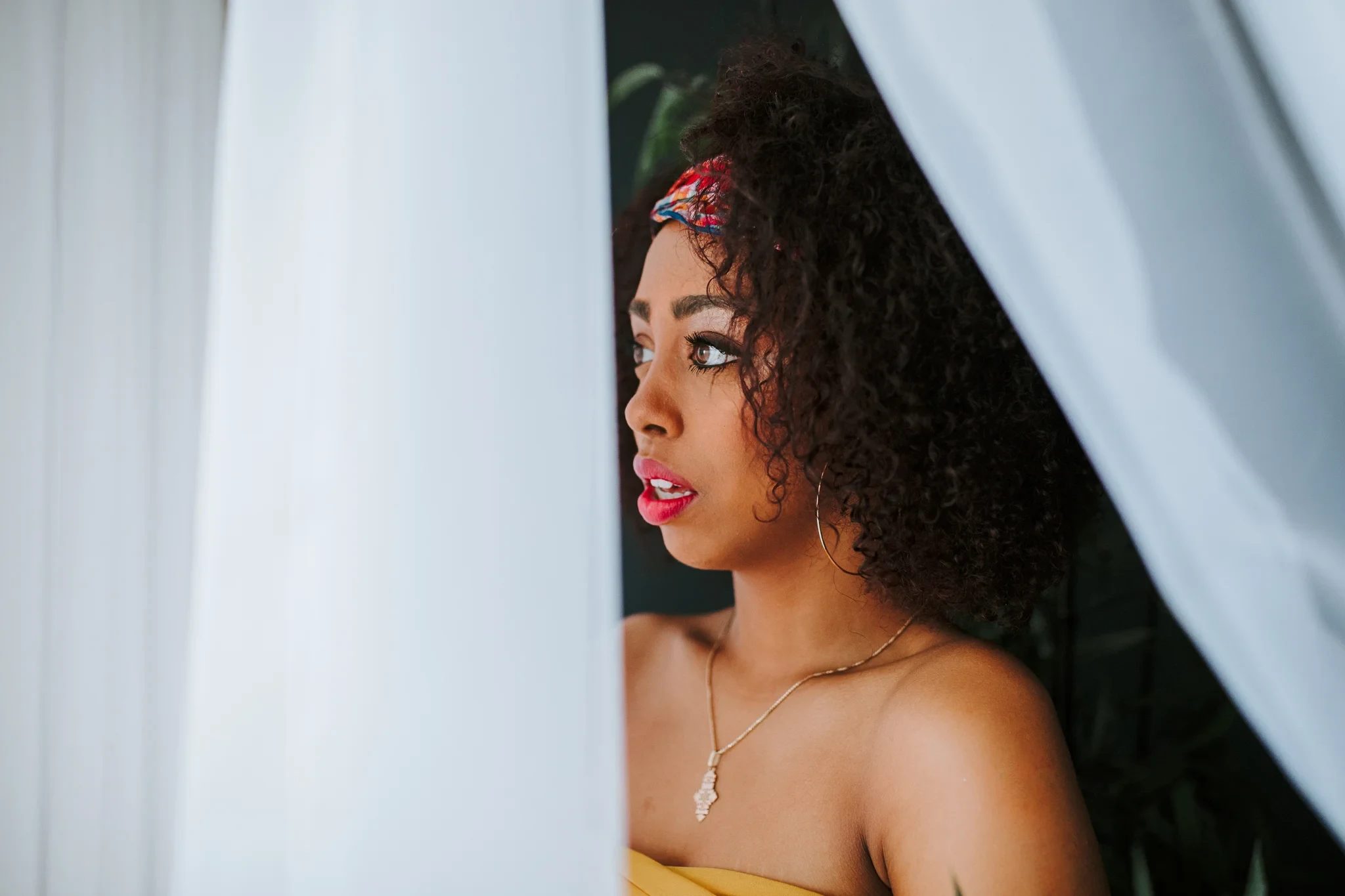 Woman looks sideways between soft white curtains