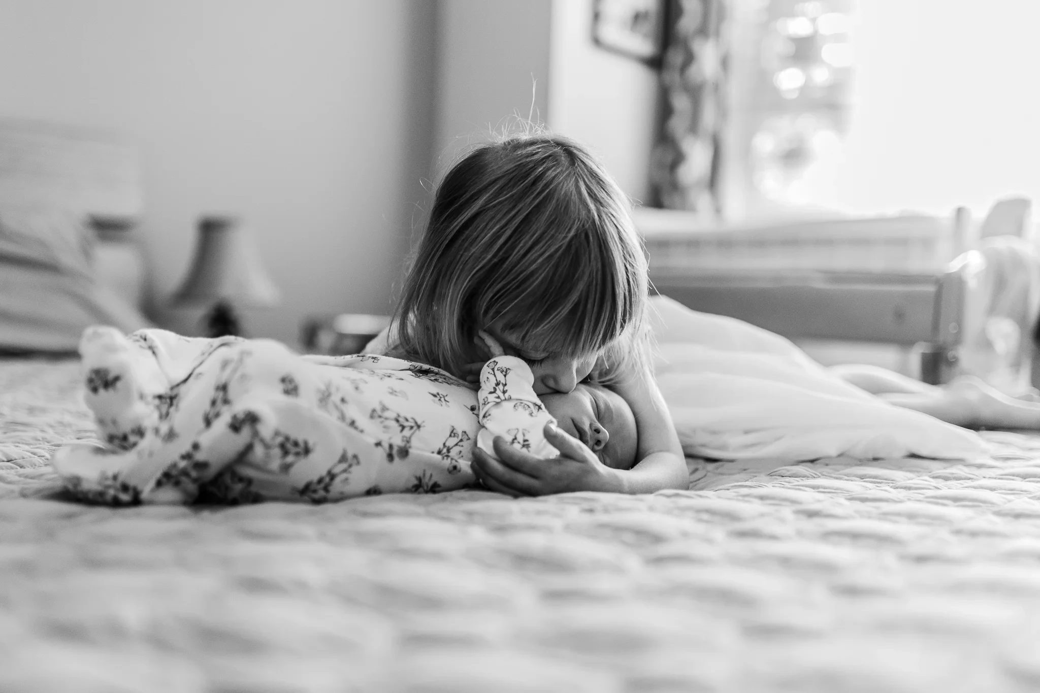 Black-and-white photograph of a child leaning over a baby on a bed
